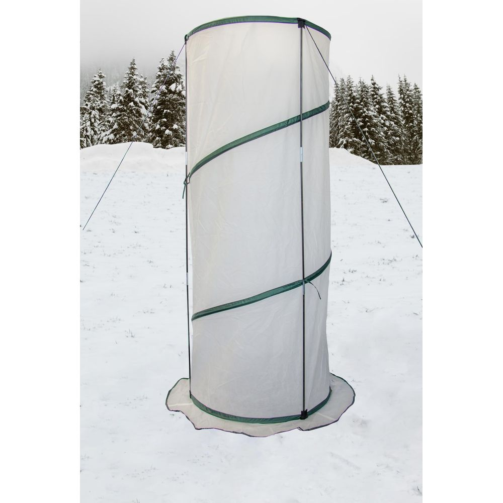 Ein weißes, zylindrisches Zelt mit grünen Streifen steht im Schnee neben Bäumen.