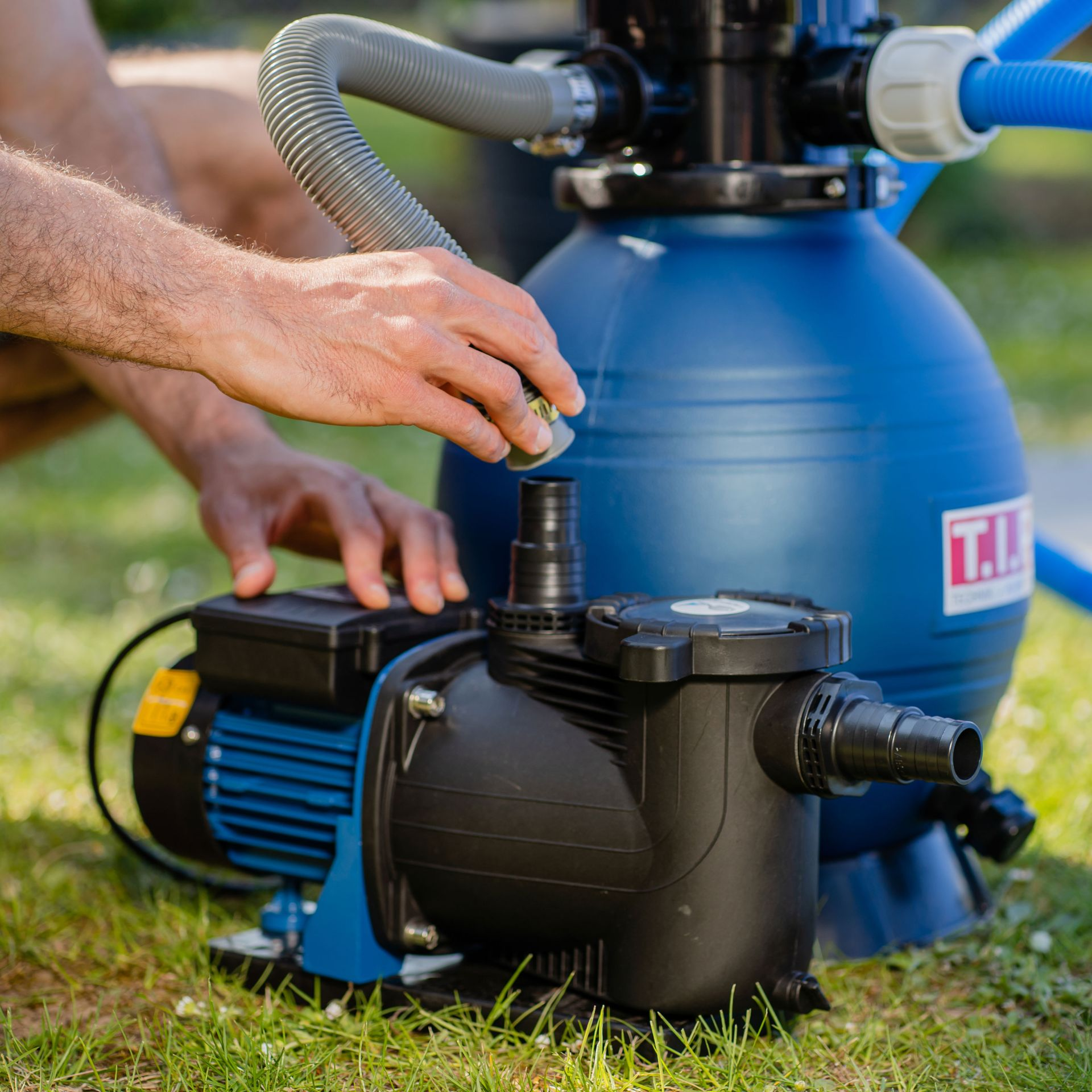 Ein Mann verbindet einen Schlauch mit einer blauen Poolpumpe auf dem Rasen.