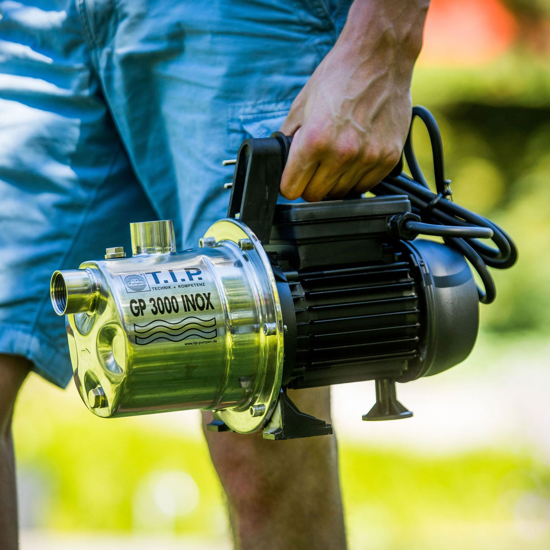 Person in blauer Hose hält eine Edelstahlpumpe mit schwarzem Motor.