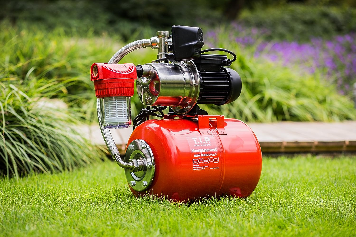 Eine rote Hauswasserpumpe mit silbernem Metall und schwarzem Motor auf grünem Gras.