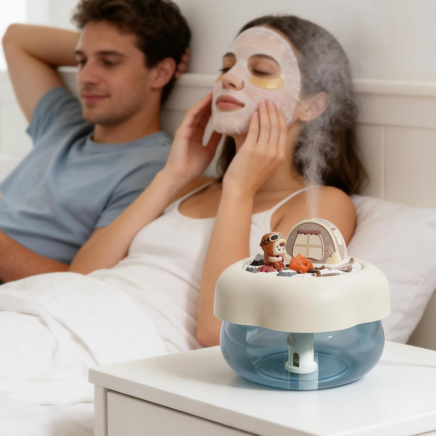Ein Paar im Bett, eine Frau mit Gesichtsmaske, ein Mann entspannt sich, ein Luftbefeuchter gibt Dampf ab.