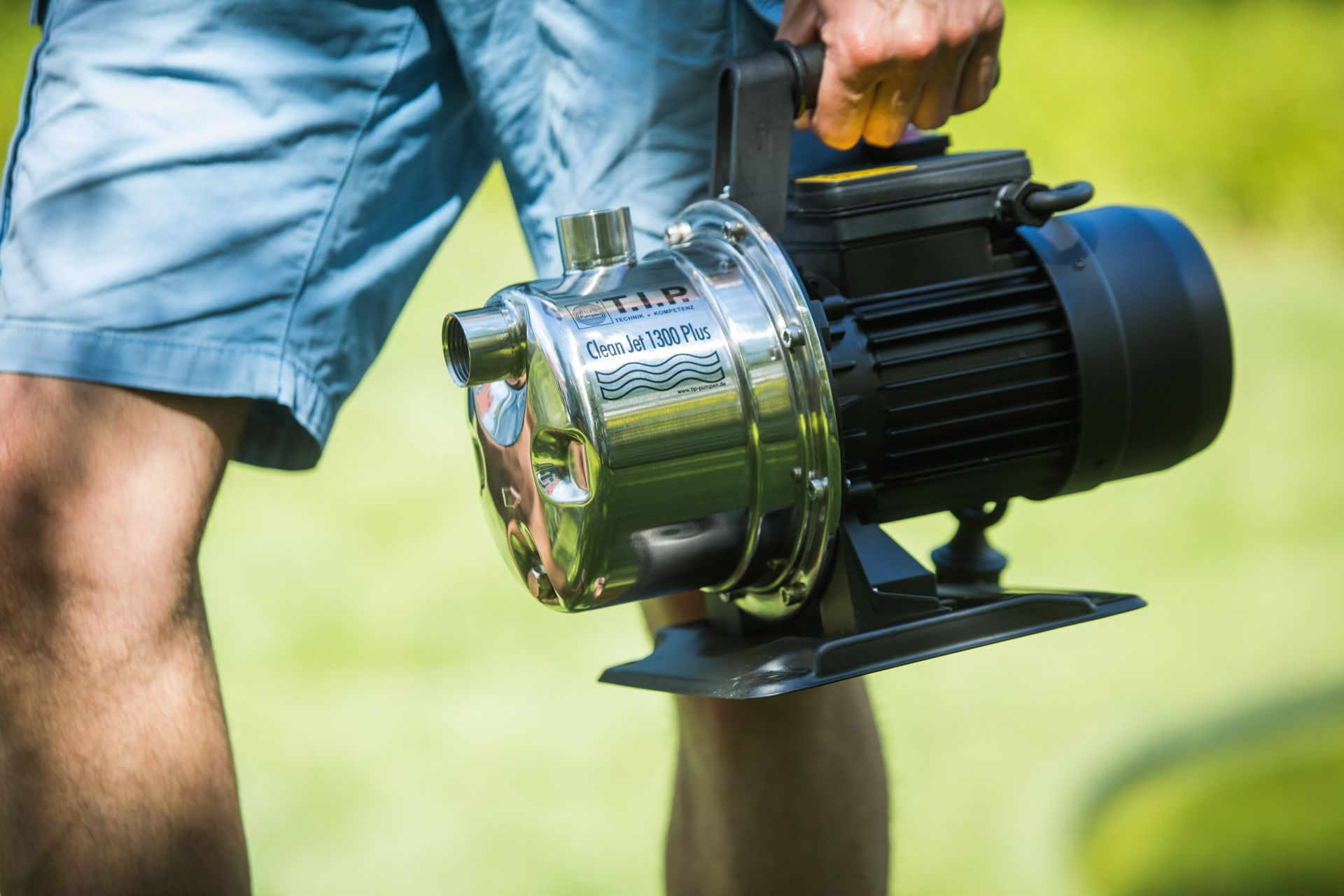 Mann in blauen Shorts hält eine glänzende Wasserpumpe mit schwarzem Motor.