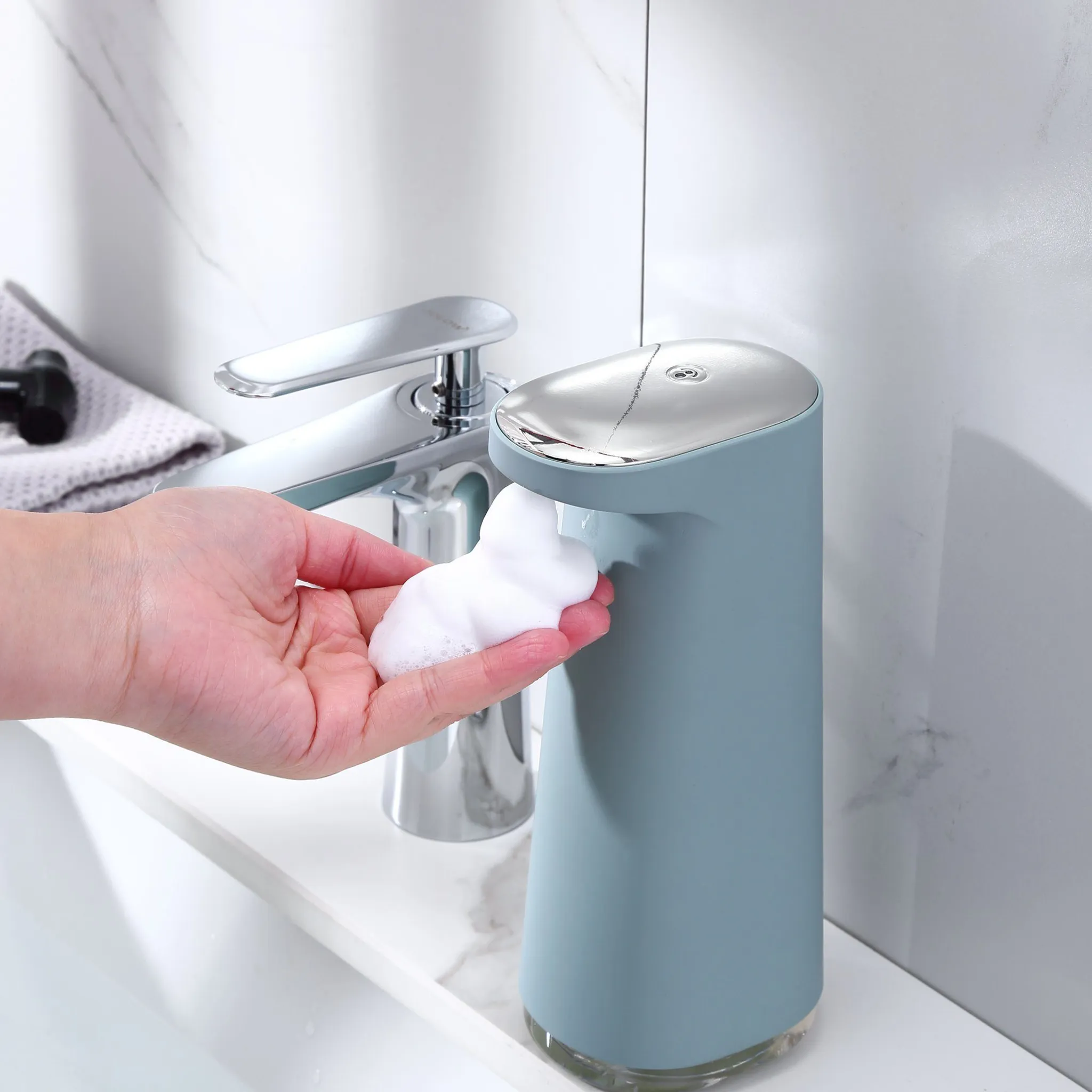 Eine Hand fängt Schaum von einem blauen Seifenspender auf. Ein Wasserhahn ist im Hintergrund.