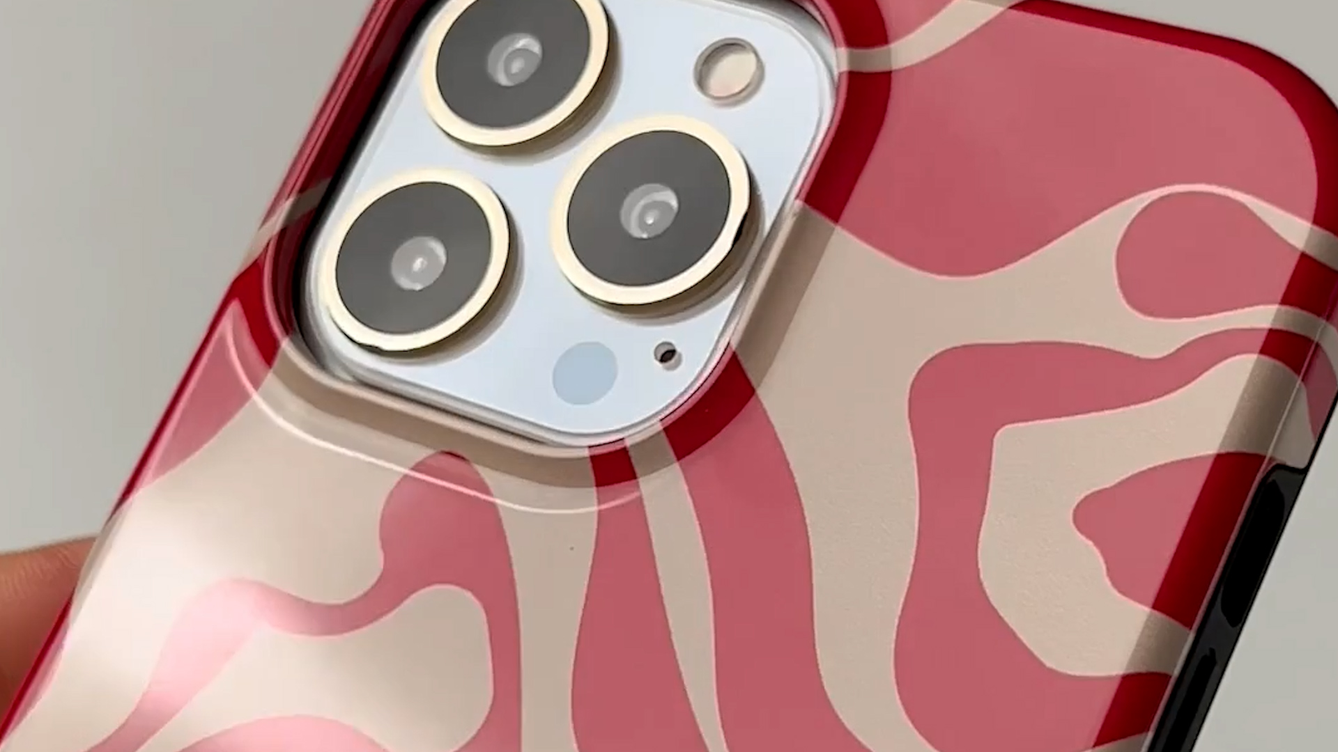 Coque de téléphone à motif ondulé rouge et crème, gros plan des trois caméras.