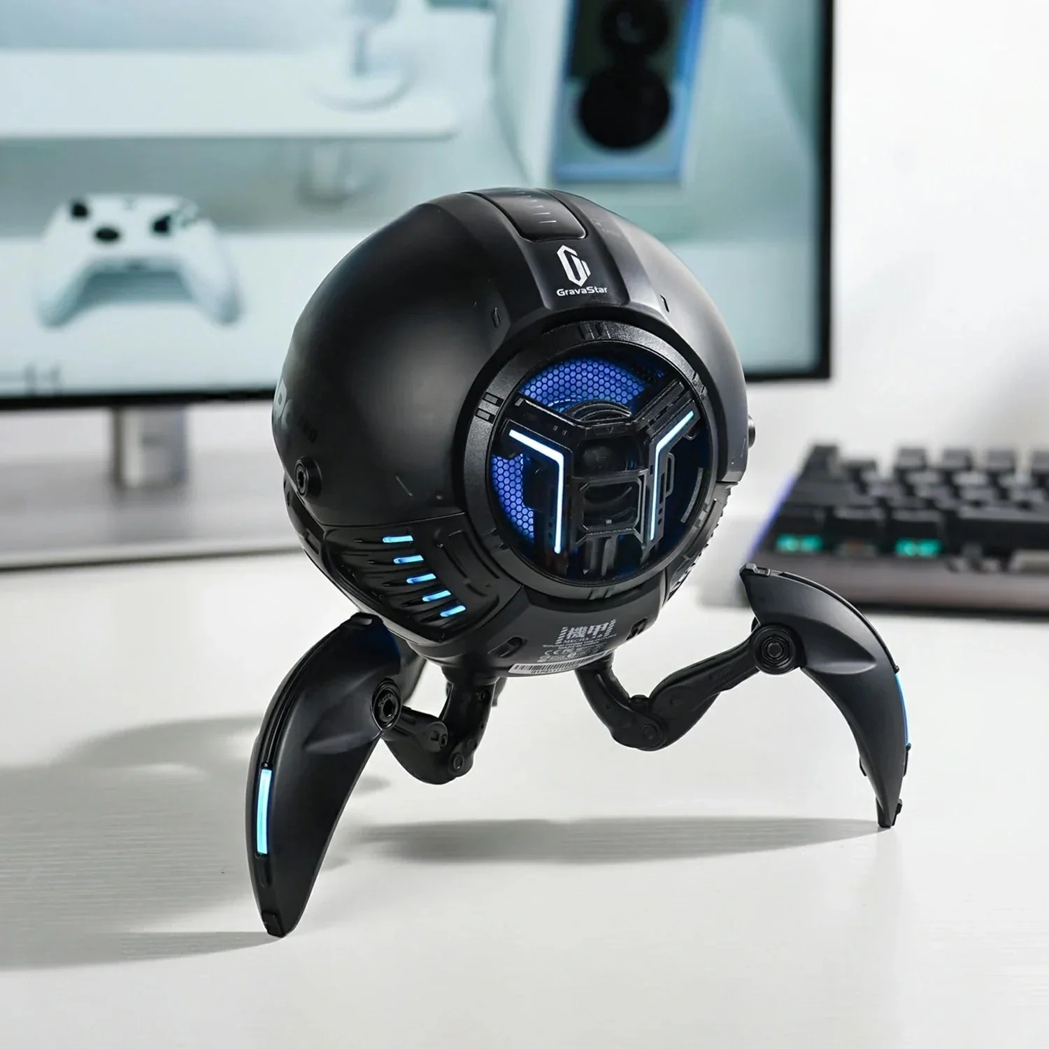 Czarny kulisty głośnik z trzema przegubowymi nogami, niebieskimi światłami, na białym biurku.