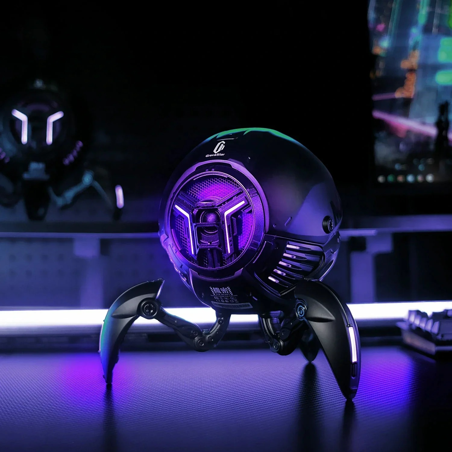 Czarny głośnik w kształcie pająka z fioletowymi światłami stoi na biurku.