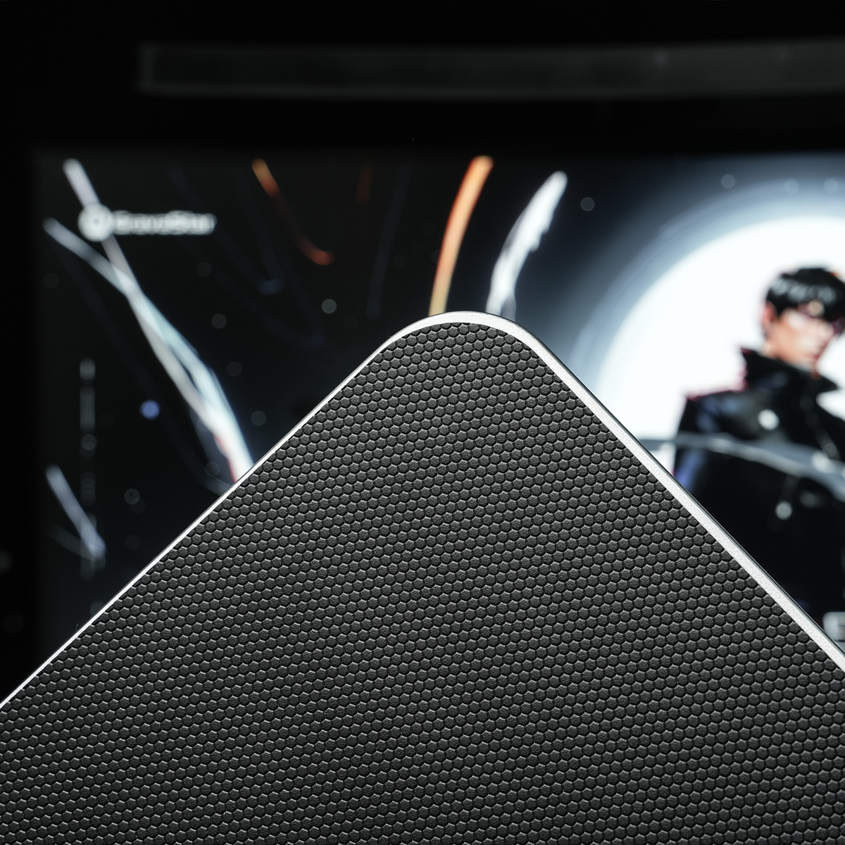 Zbliżenie czarnej kratki głośnika z srebrną krawędzią. Z tyłu widoczny jest niewyraźny obraz mężczyzny na ekranie.