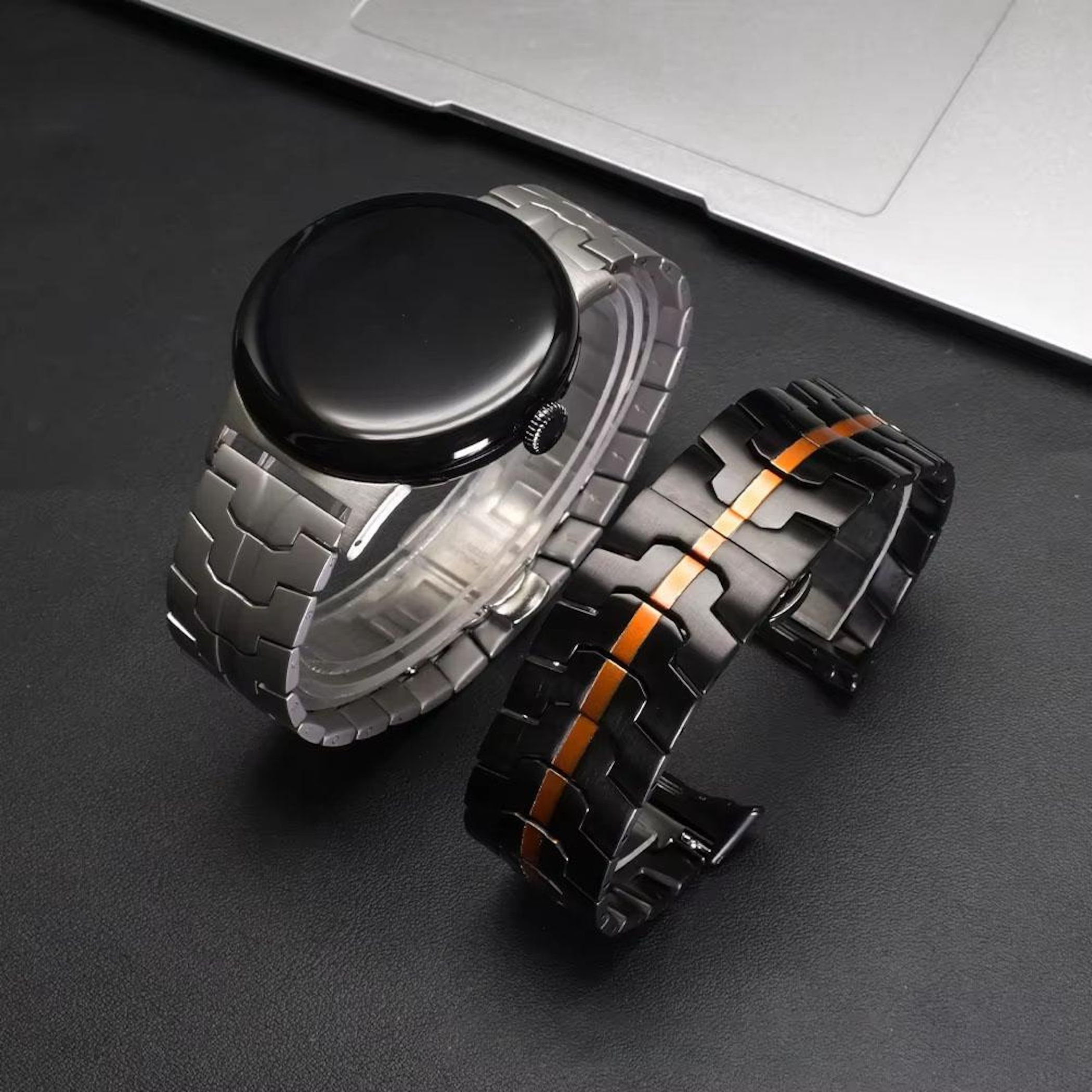 Eine schwarze Smartwatch mit silbernem Armband und ein schwarzes Armband mit orangefarbener Linie.