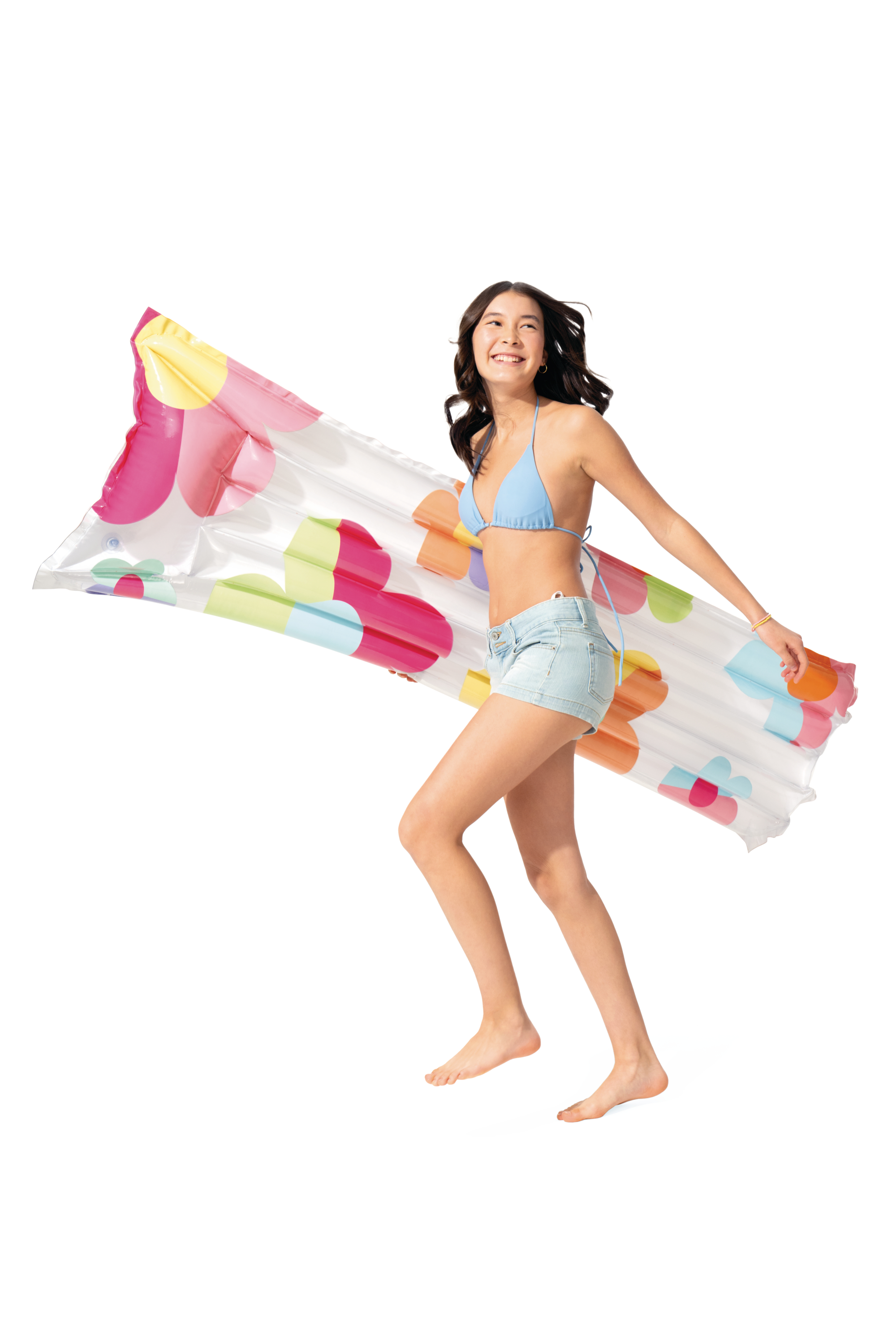 Kobieta w bikini i dżinsowych szortach niesie dmuchany materac w kwiaty.