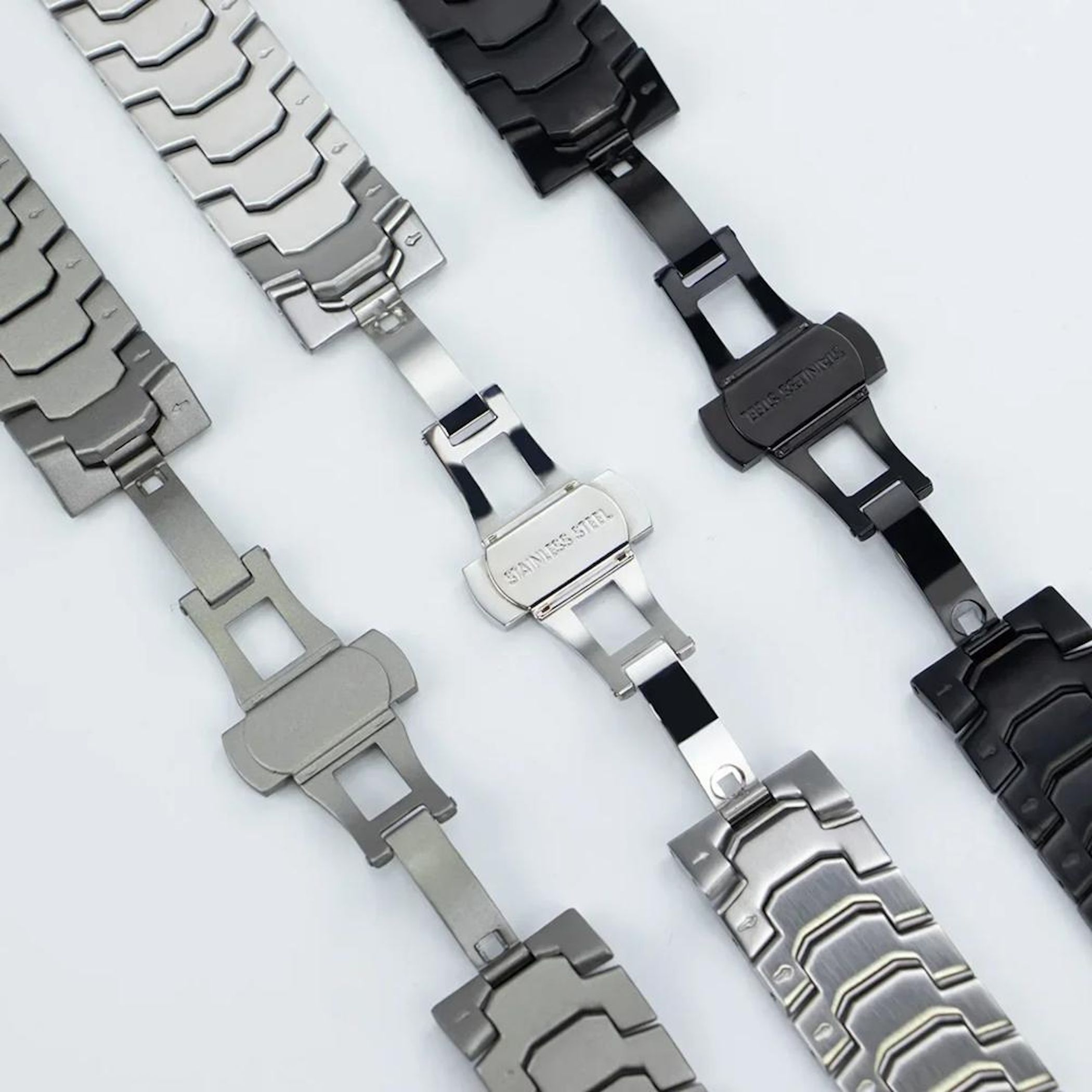 Tre cinturini per orologi in acciaio inossidabile argento e neri con fibbie.