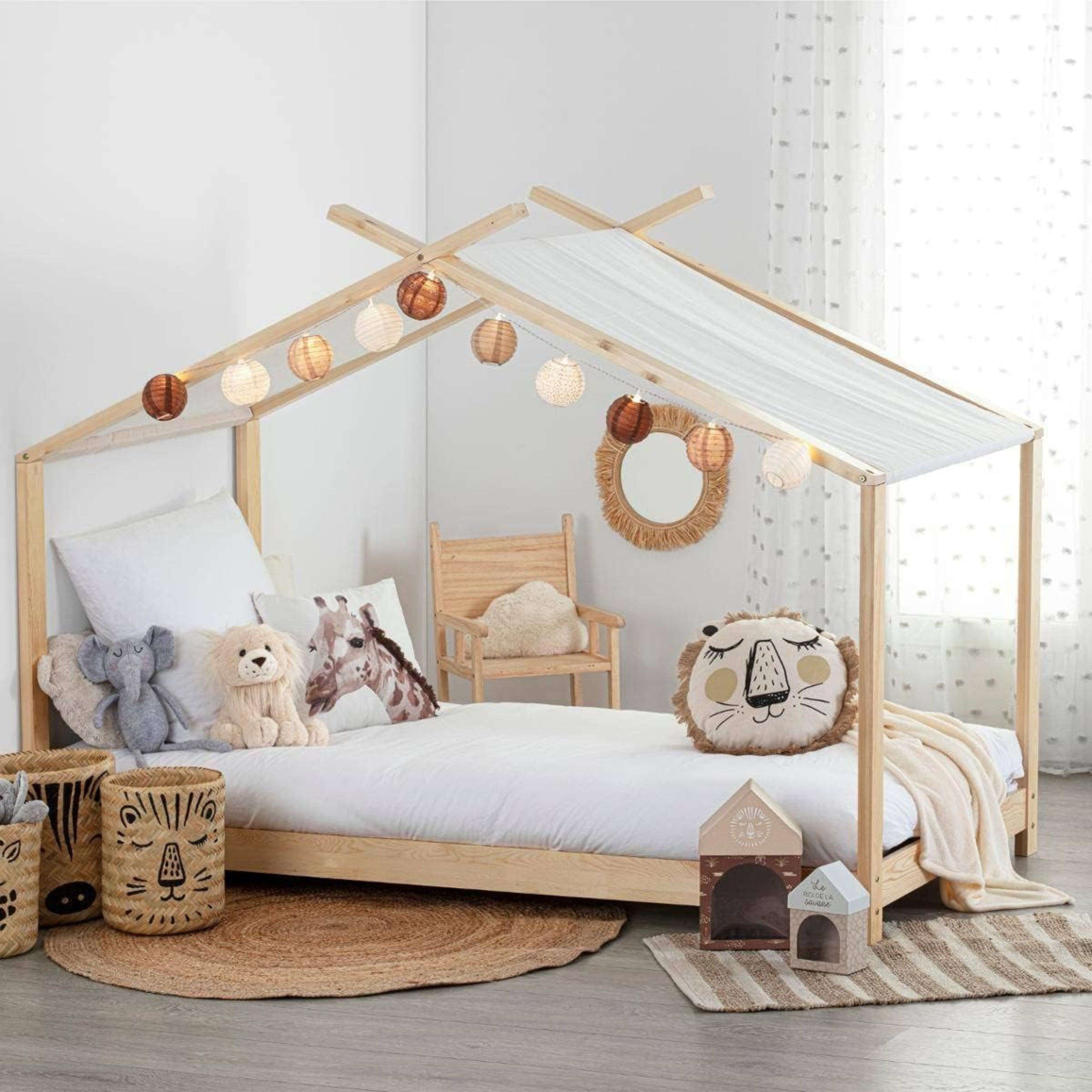 Una cama infantil de madera con ropa de cama, peluches y luces de hilo.