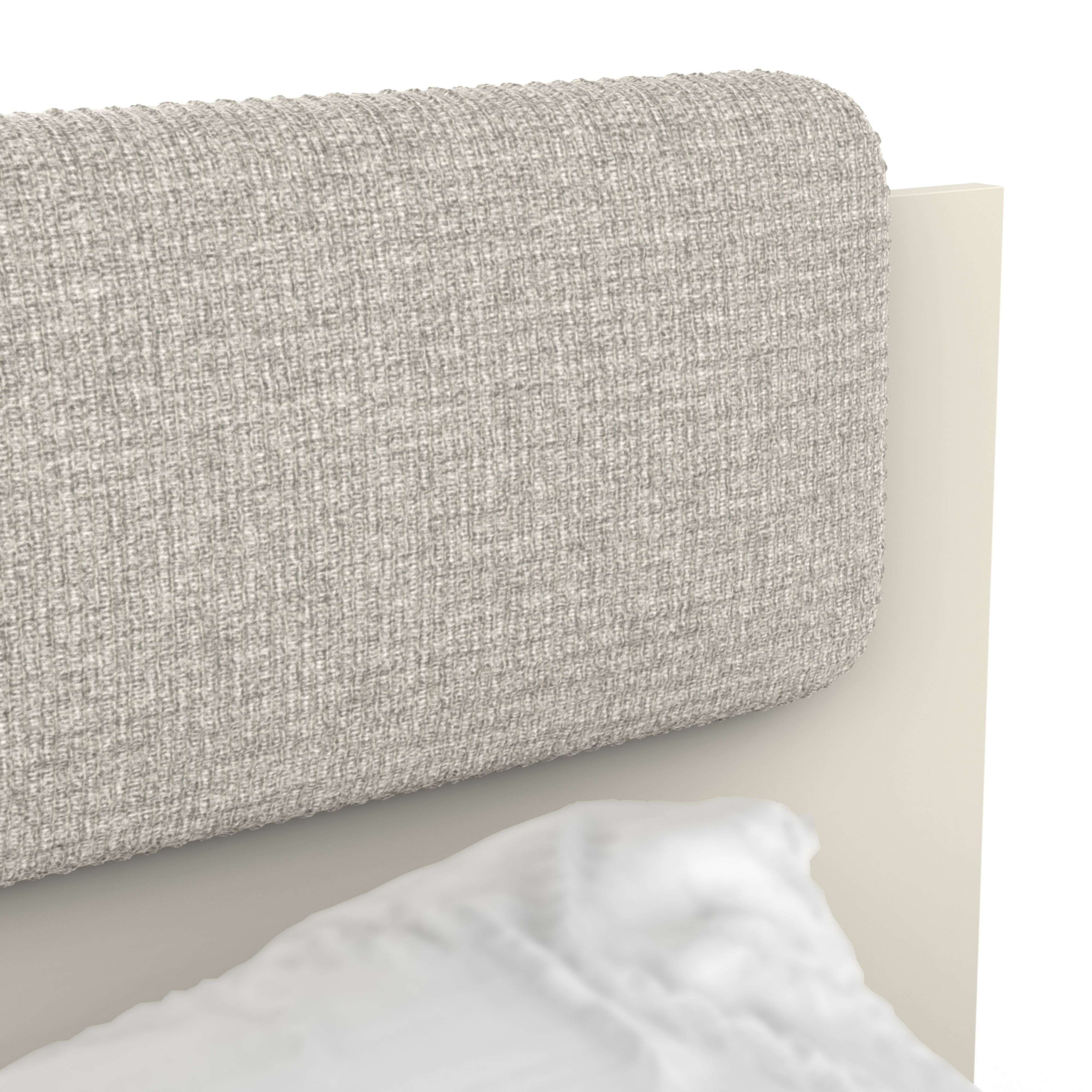 Un cabecero gris tapizado con una almohada blanca delante.