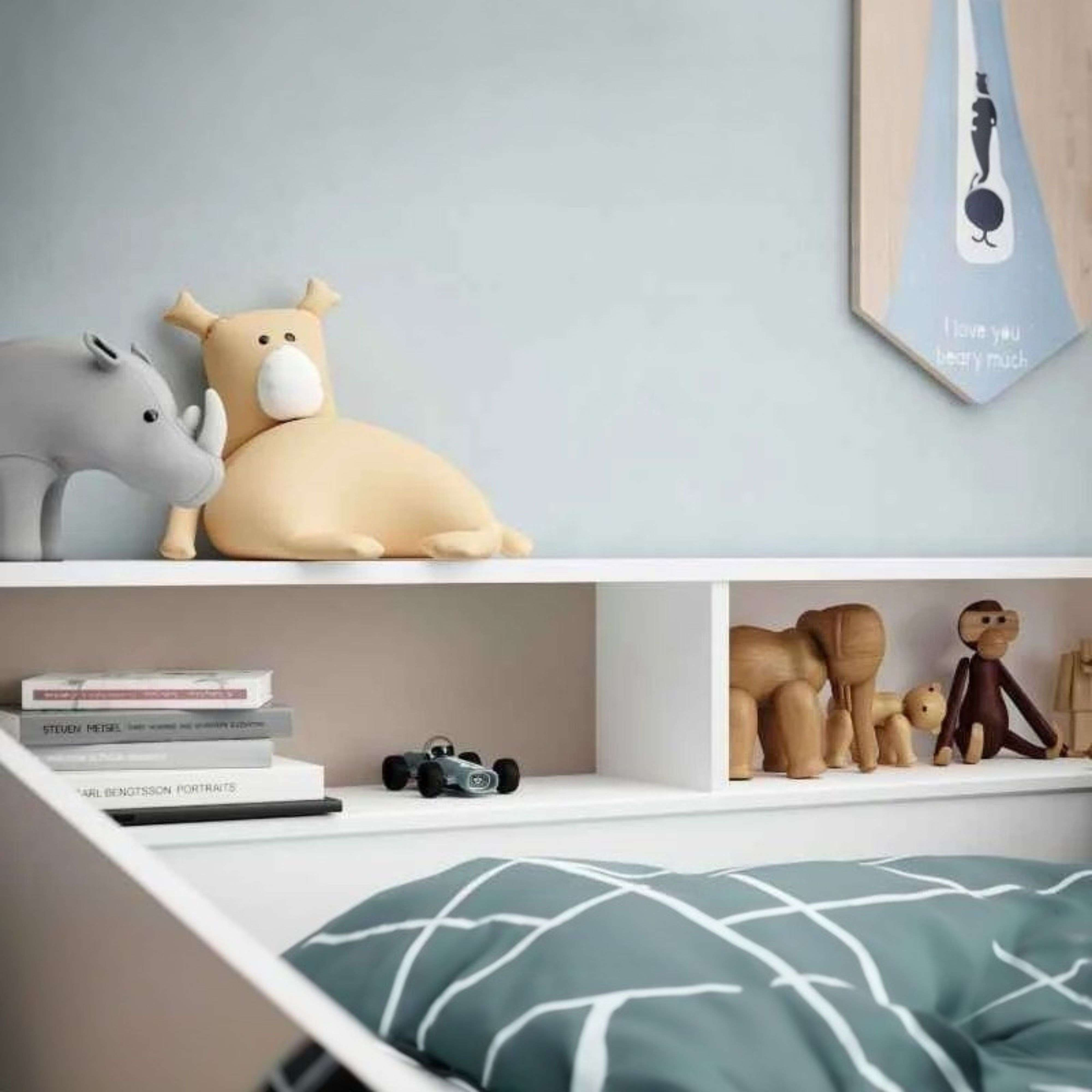 Un estante con juguetes y libros. Un peluche de rinoceronte y oso, figuras de animales de madera, un coche de juguete y libros.
