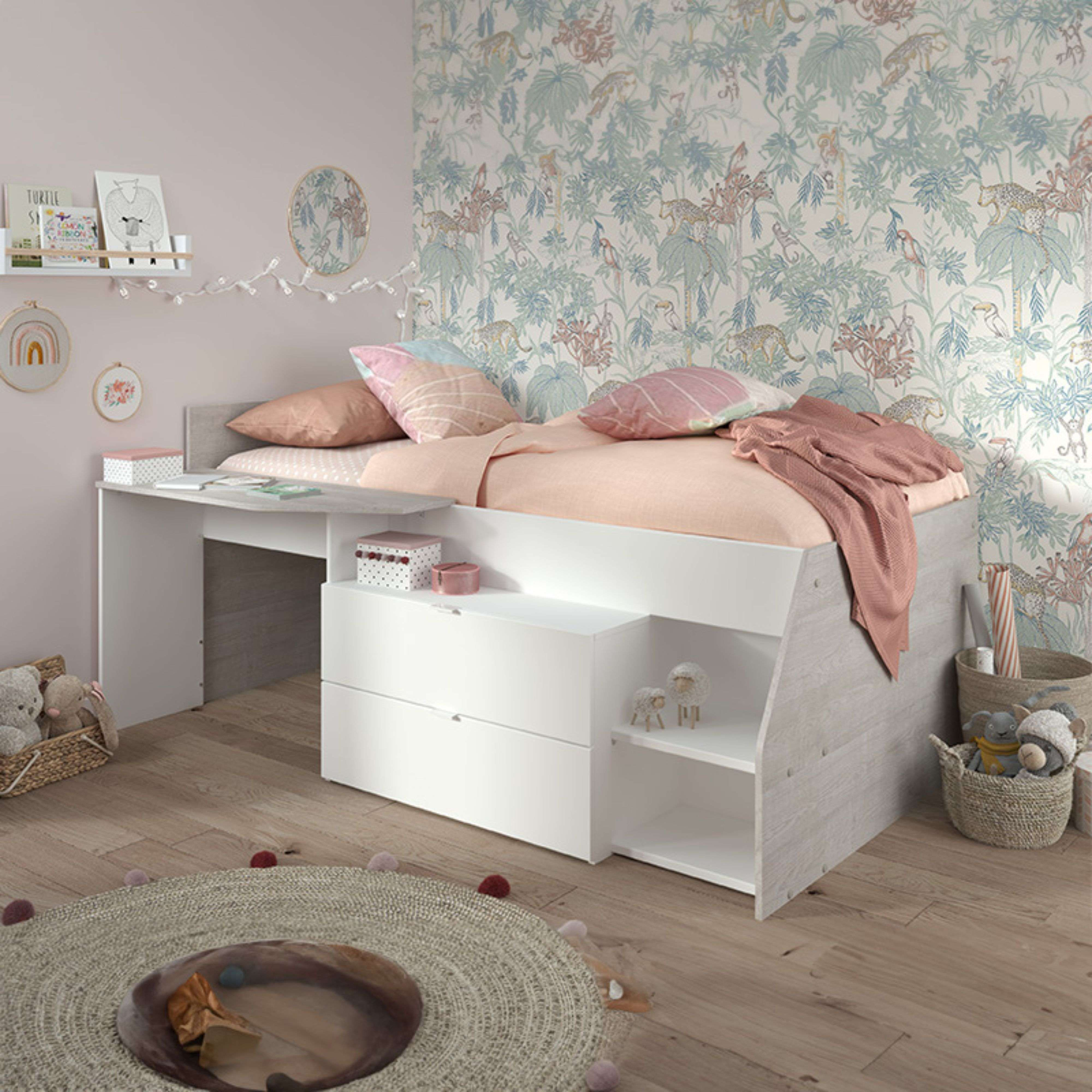 Una cama infantil con escritorio, cajones, cojines, manta y juguetes.