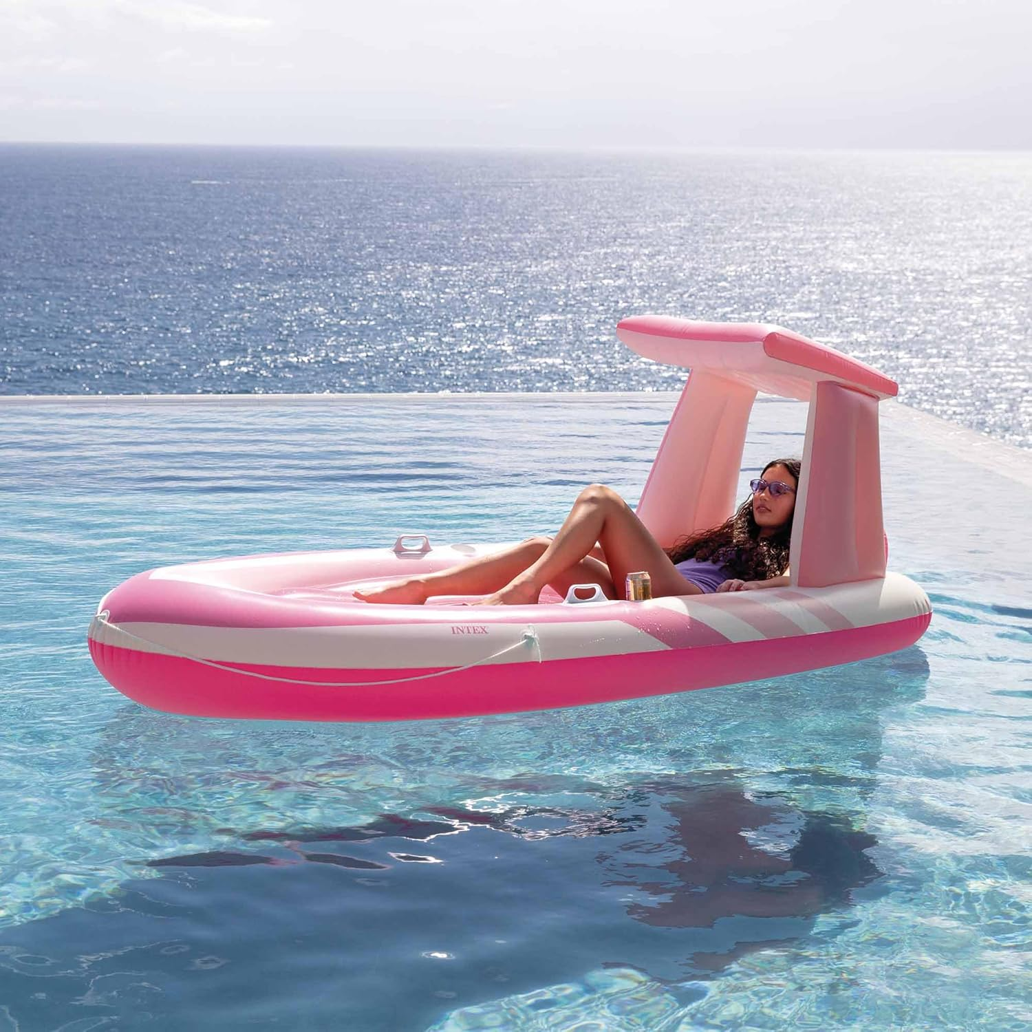 Eine Frau auf einem rosa aufblasbaren Boot mit Baldachin im Pool, mit Blick auf das Meer.
