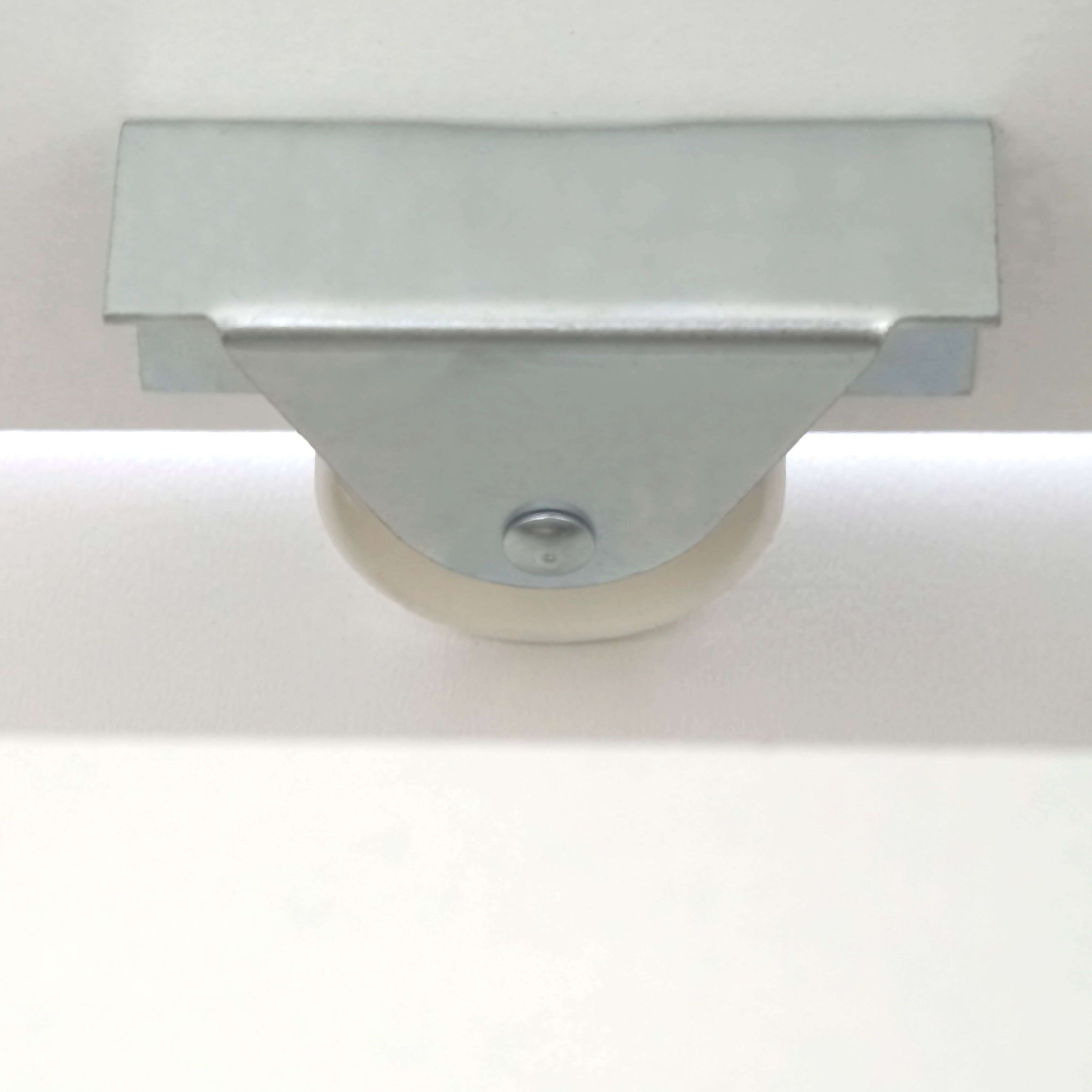 Un rodillo metálico plateado con rueda blanca sobre superficie blanca.