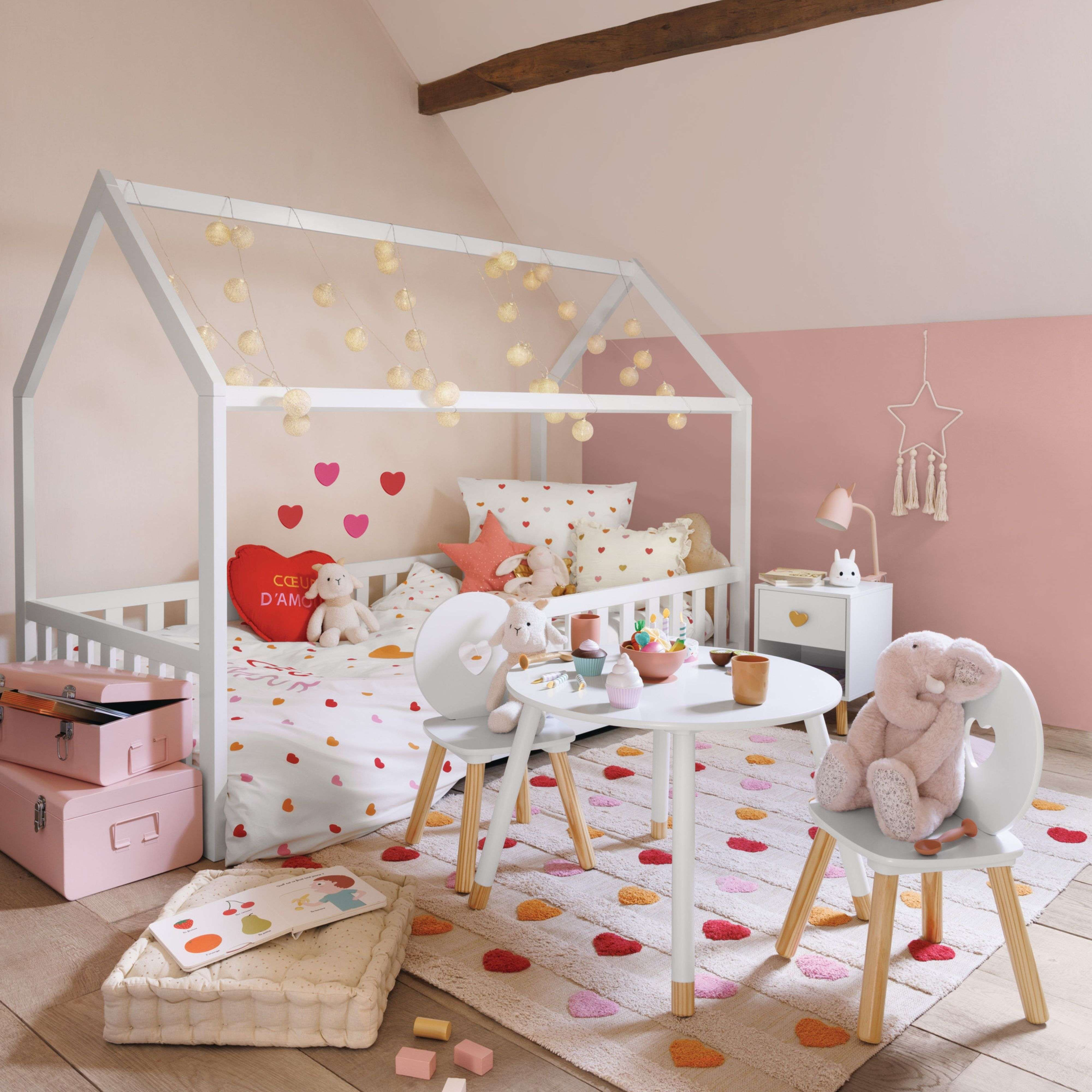 Habitación infantil con cama casita, luces, decoración de corazones, juguetes y mesa.