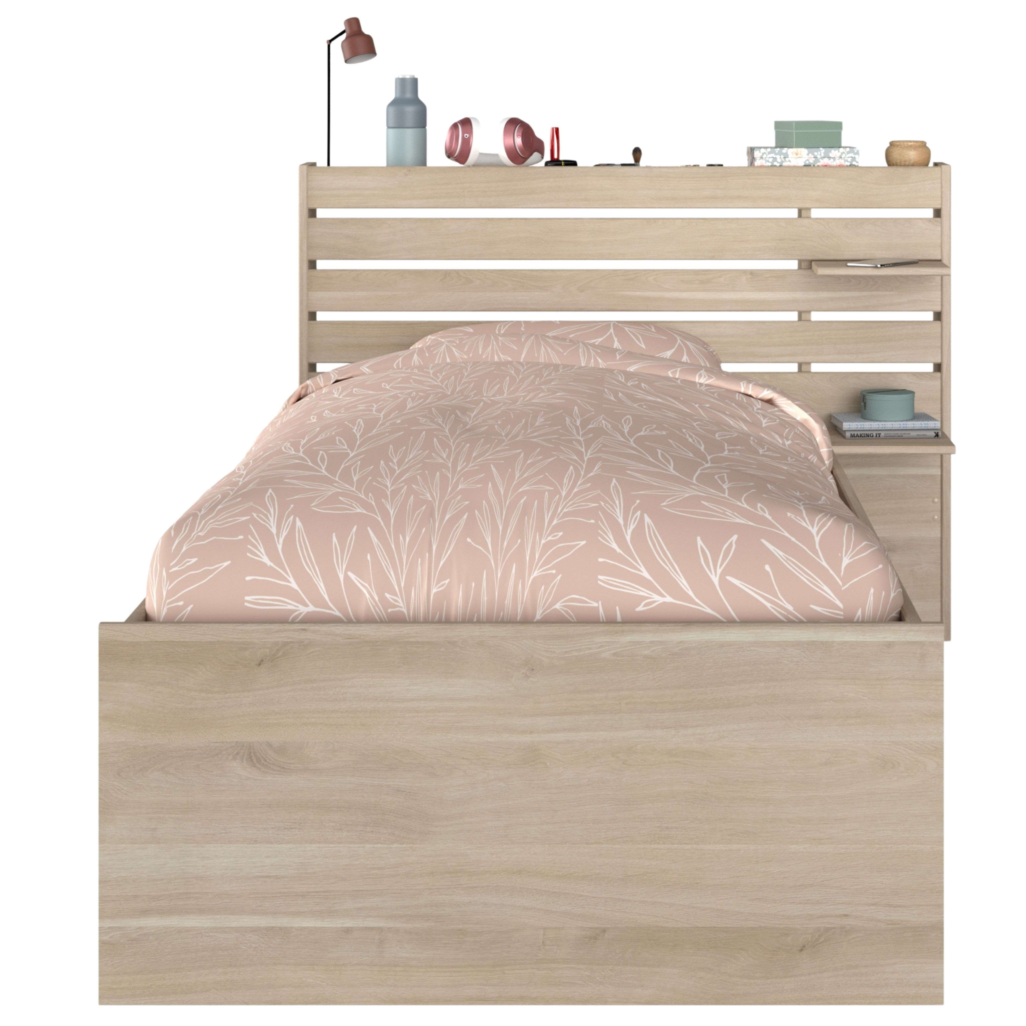Una cama de madera con edredón estampado de hojas. Artículos decorativos en el cabecero.