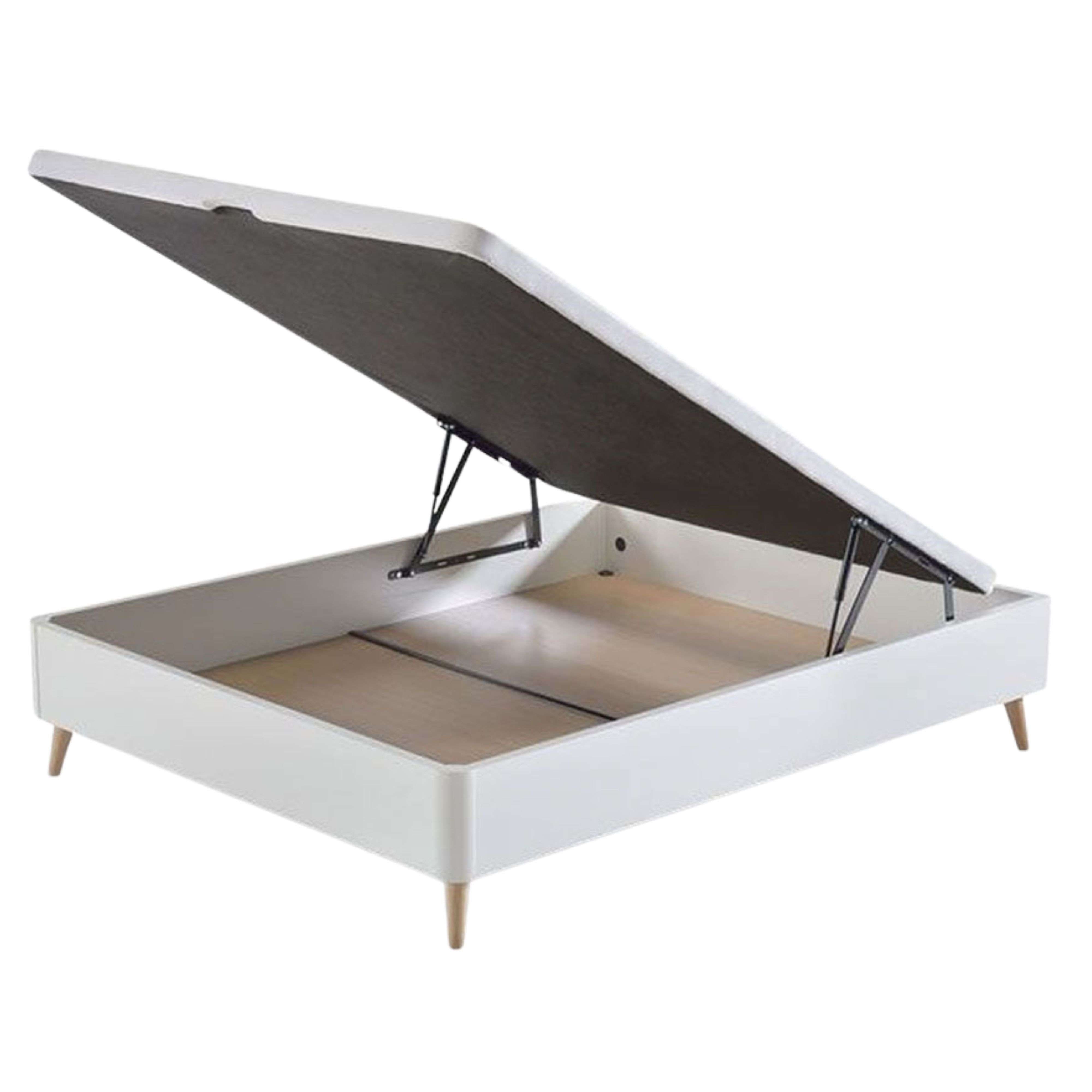 Una base de cama blanca con somier levantado y patas de madera.