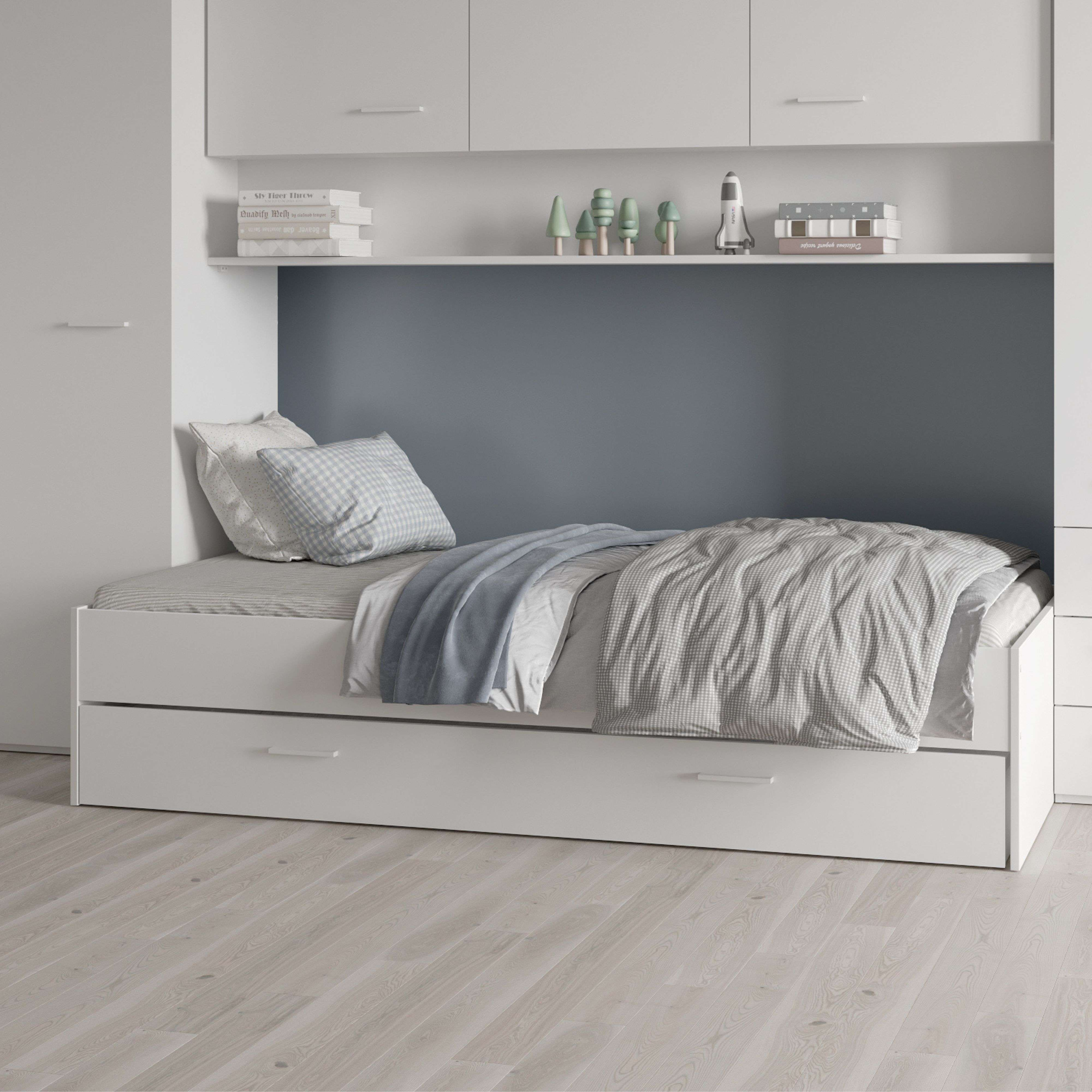 Una cama blanca con ropa de cama, mantas y almohadas. Las estanterías tienen libros, árboles y un cohete.