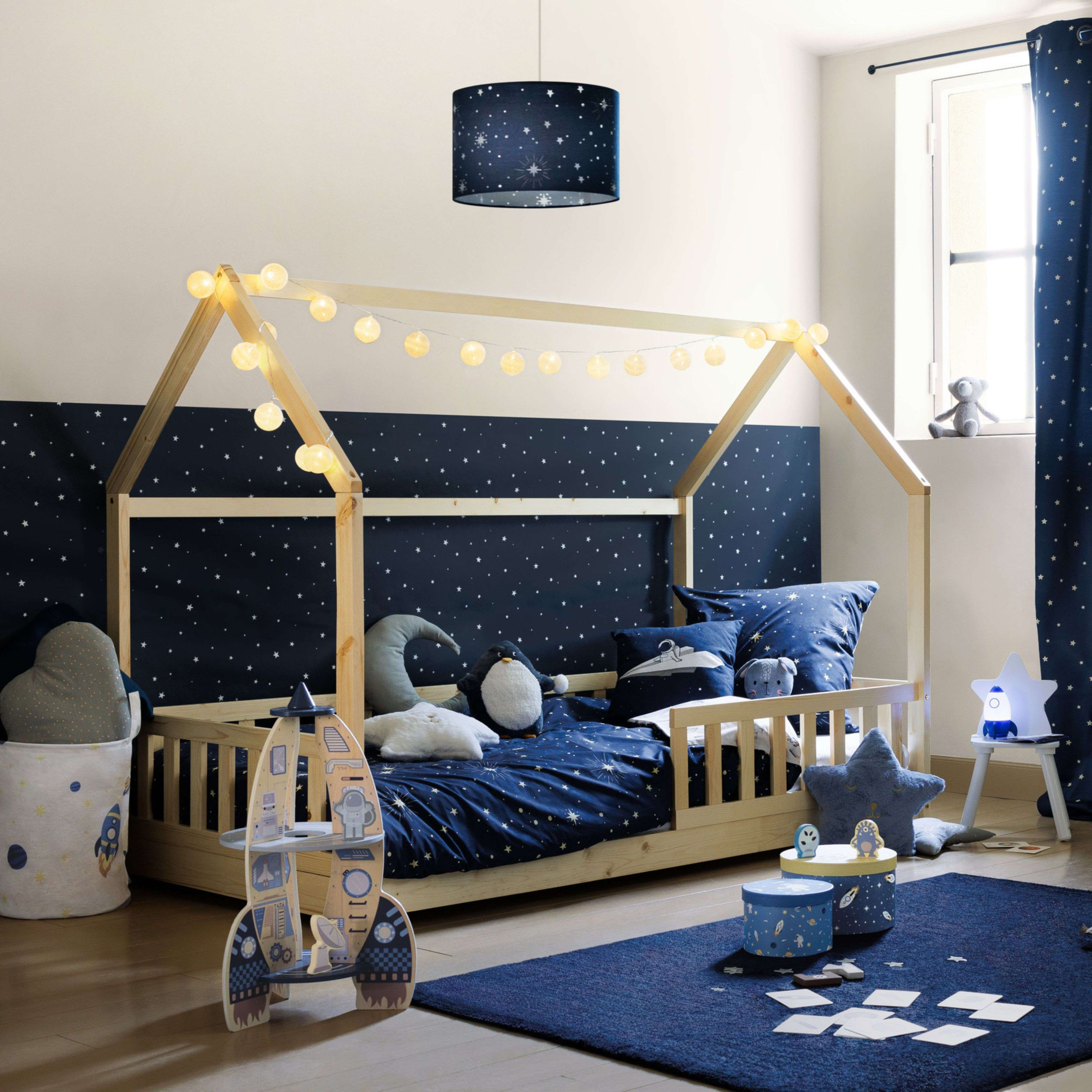 Habitación infantil temática espacial: cama, cohete de juguete, lámpara, oso en alféizar.