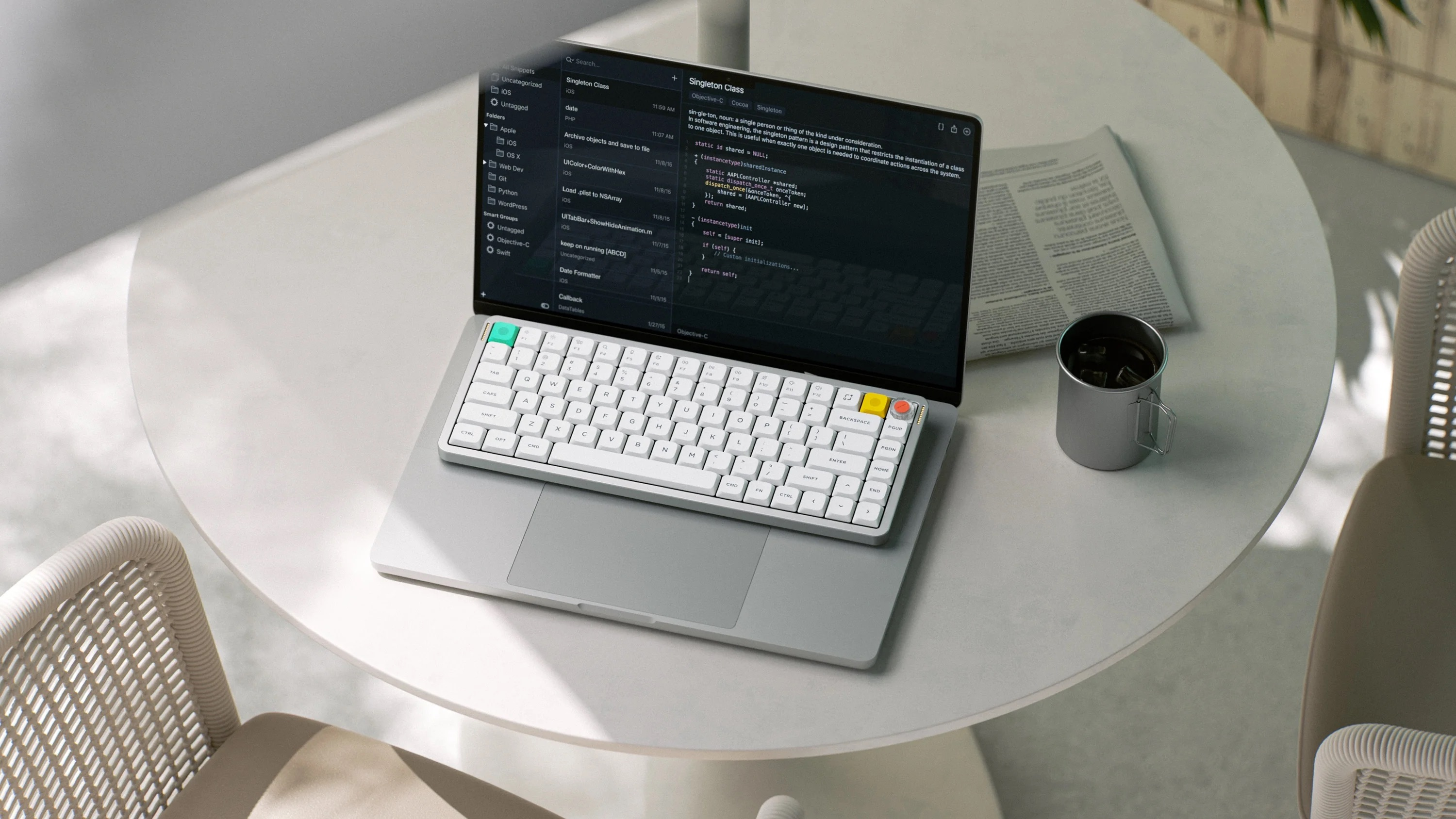 Otwarty laptop z klawiaturą, kubkiem i gazetą na stole.