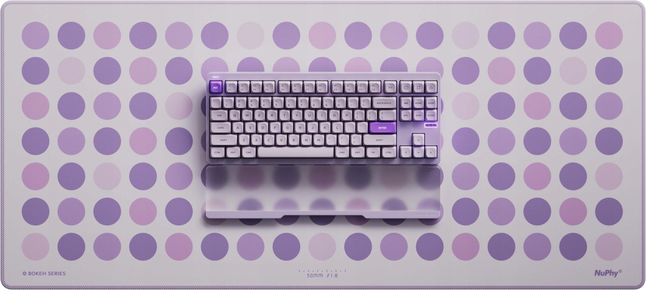 Fioletowa klawiatura mechaniczna i podpórka pod nadgarstek na macie z fioletowymi kropkami.