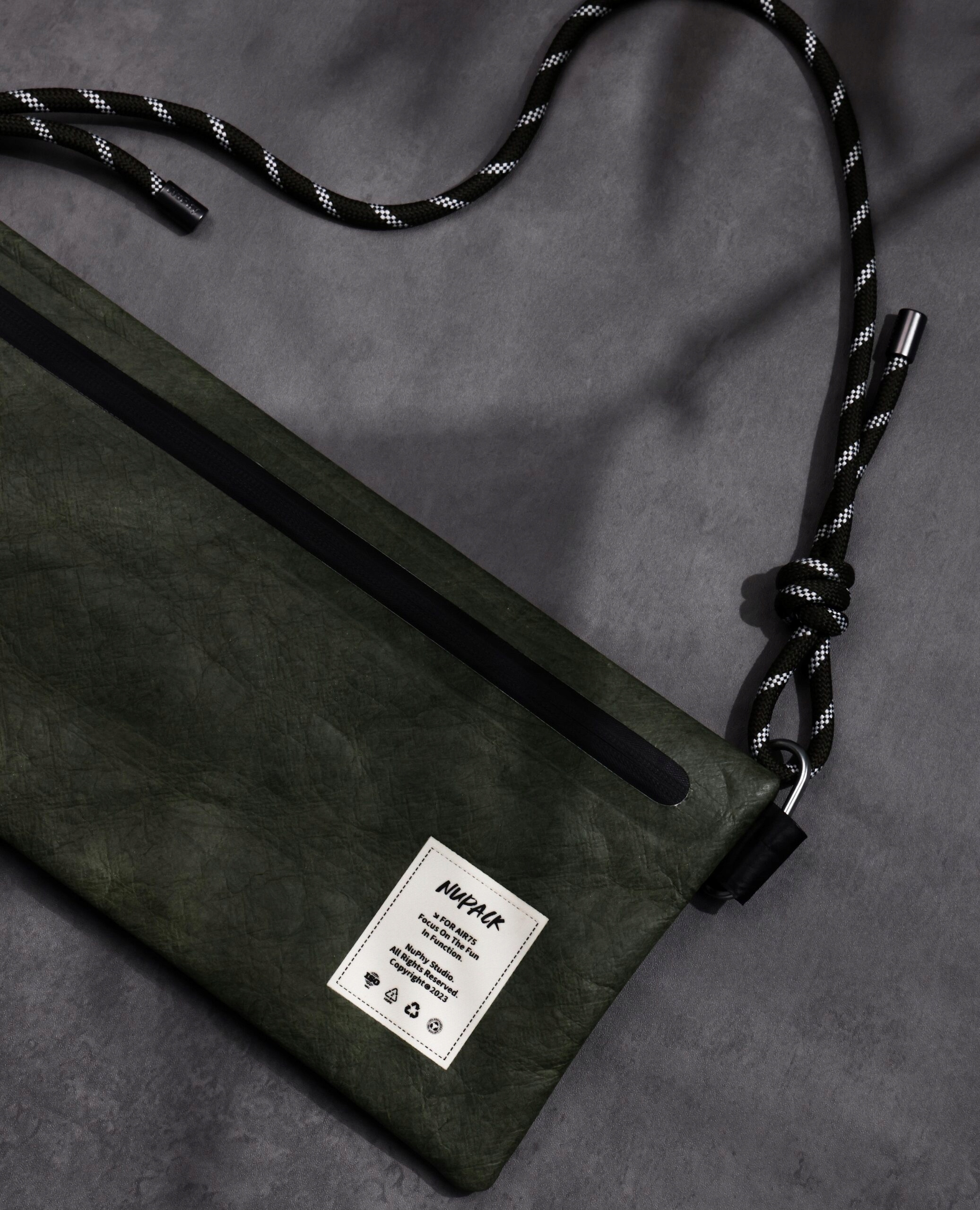 Una borsa verde con cerniera nera e tracolla in corda su sfondo grigio.