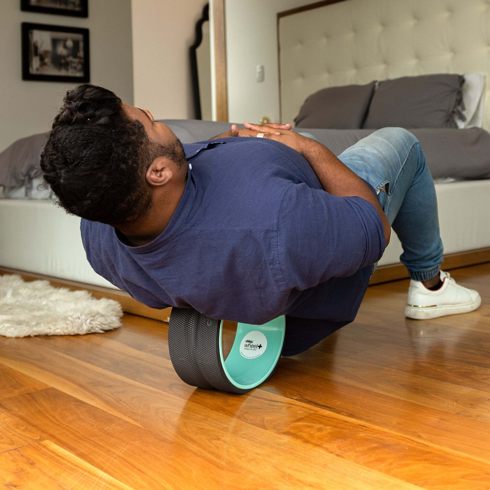 Uomo sdraiato su una ruota yoga su pavimento in legno davanti a letto.