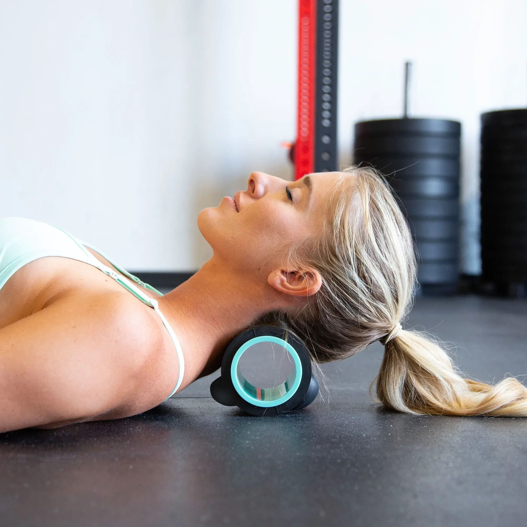 Eine Frau liegt auf dem Boden und benutzt eine Nackenrolle im Fitnessstudio.