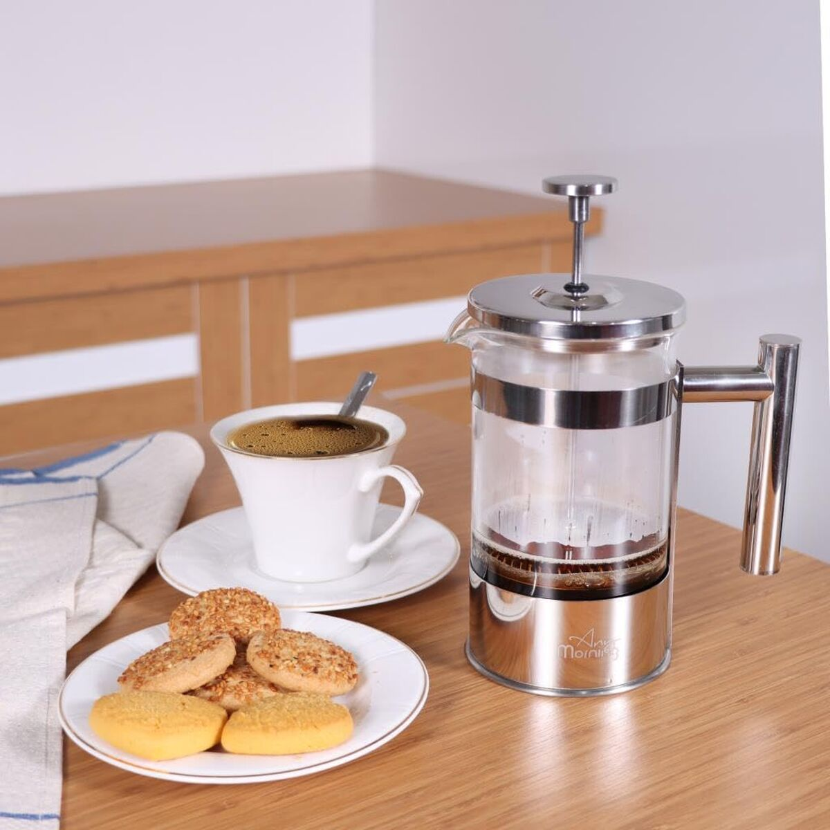 Una taza de café, galletas y una prensa francesa sobre una mesa de madera.