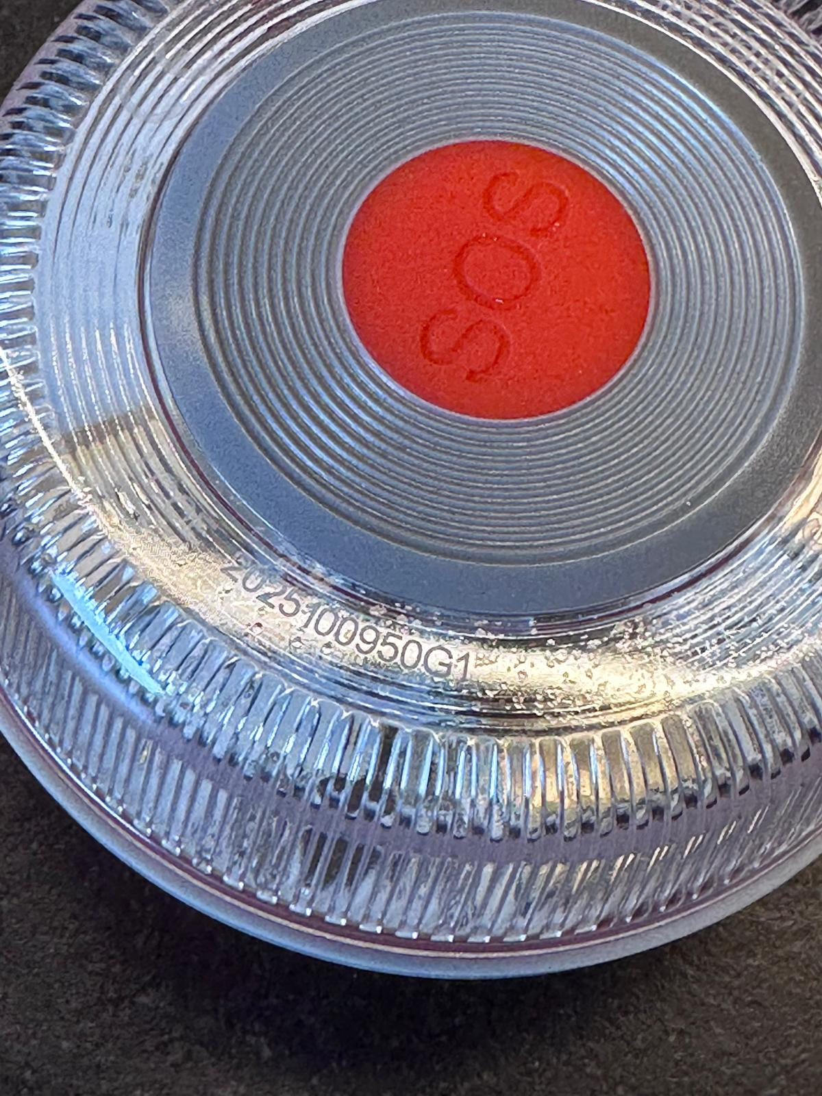 Primer plano de un dispositivo de plástico transparente y acanalado con botón SOS rojo y número de serie.