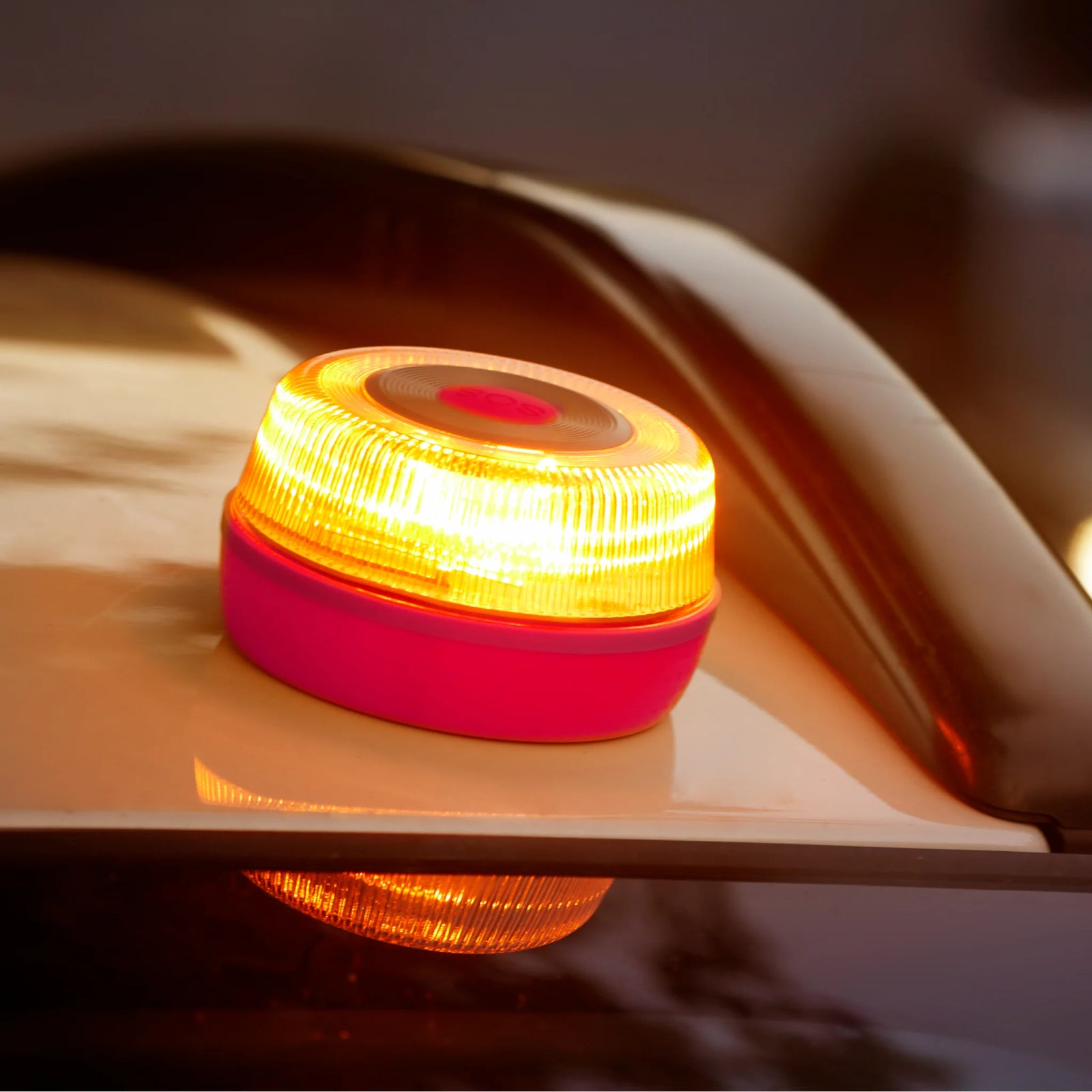 Una luz de advertencia amarilla brillante con base rosa está sobre un coche.