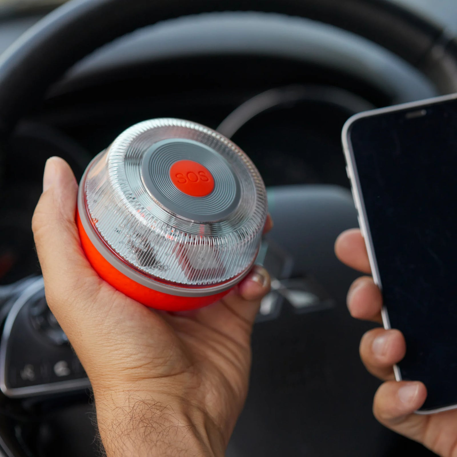 Mano sostiene luz de advertencia SOS naranja y smartphone delante del volante.