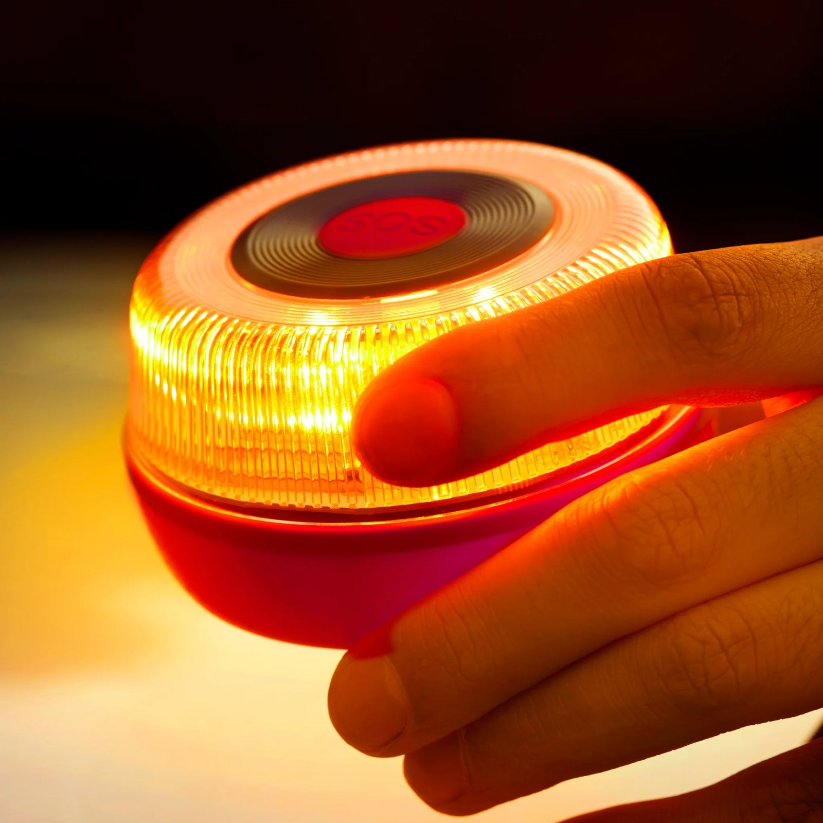 Una mano sujeta una luz SOS amarilla brillante con un botón rojo.