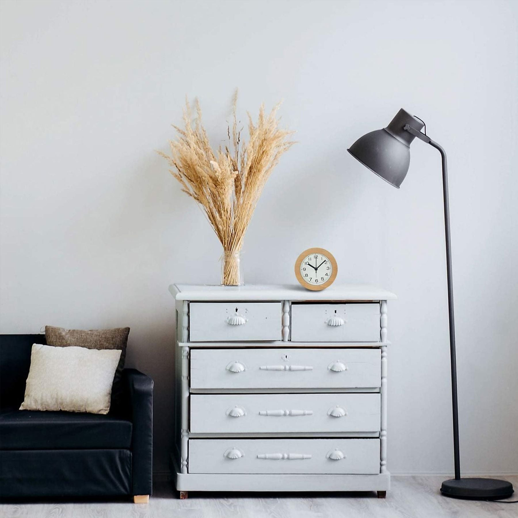 Ein Sofa, eine Kommode mit Trockenblumen und eine Stehlampe.