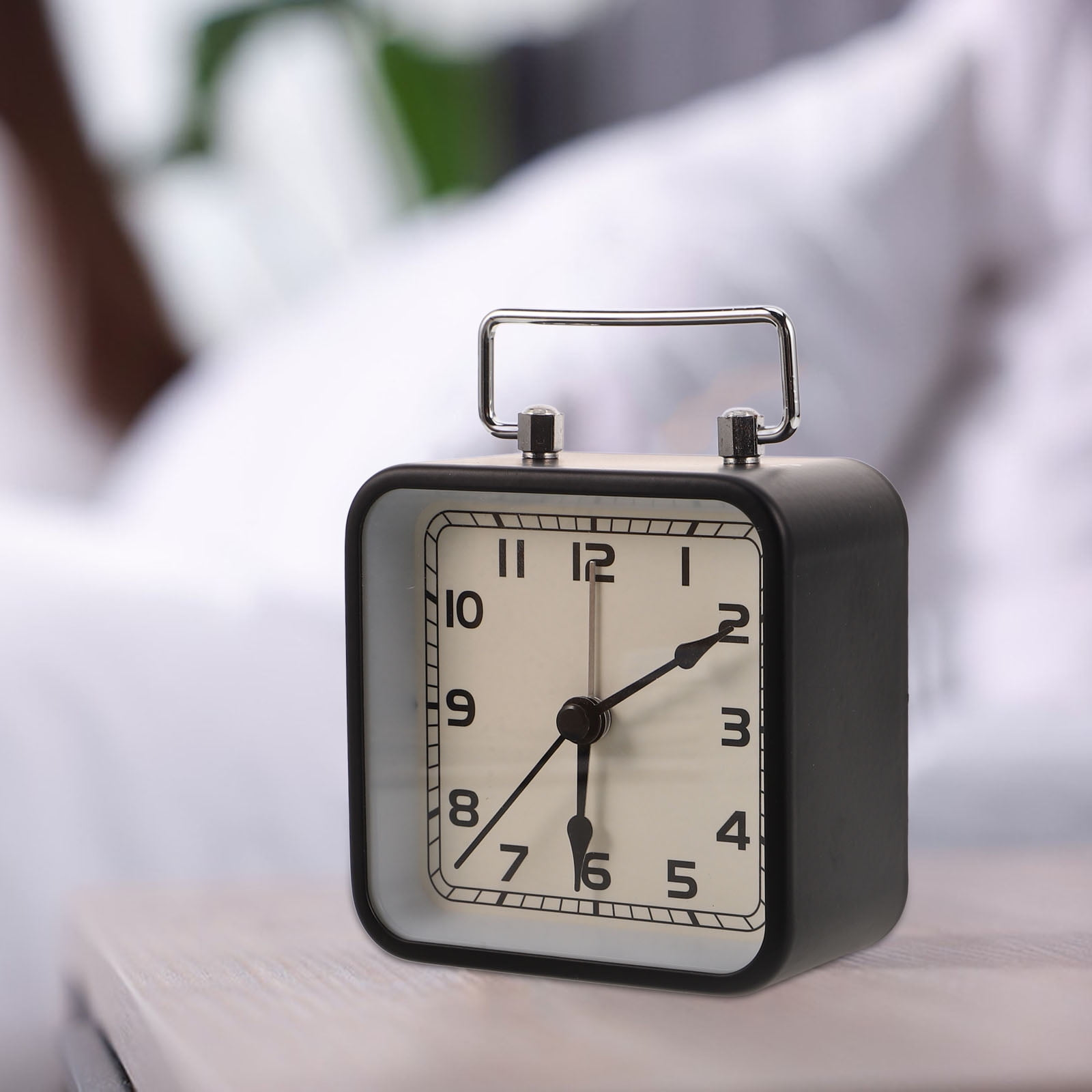 Ein schwarzer Wecker mit silbernem Griff steht auf einem Nachttisch. Es ist 6:01 Uhr.