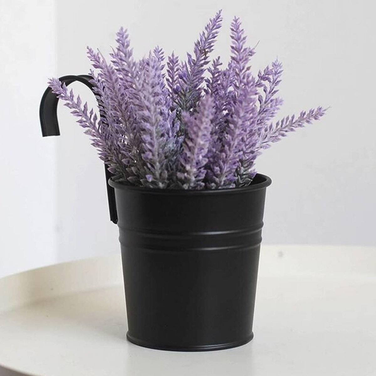 Ein schwarzer Topf mit Lavendelblüten, der an einer Wand hängt.