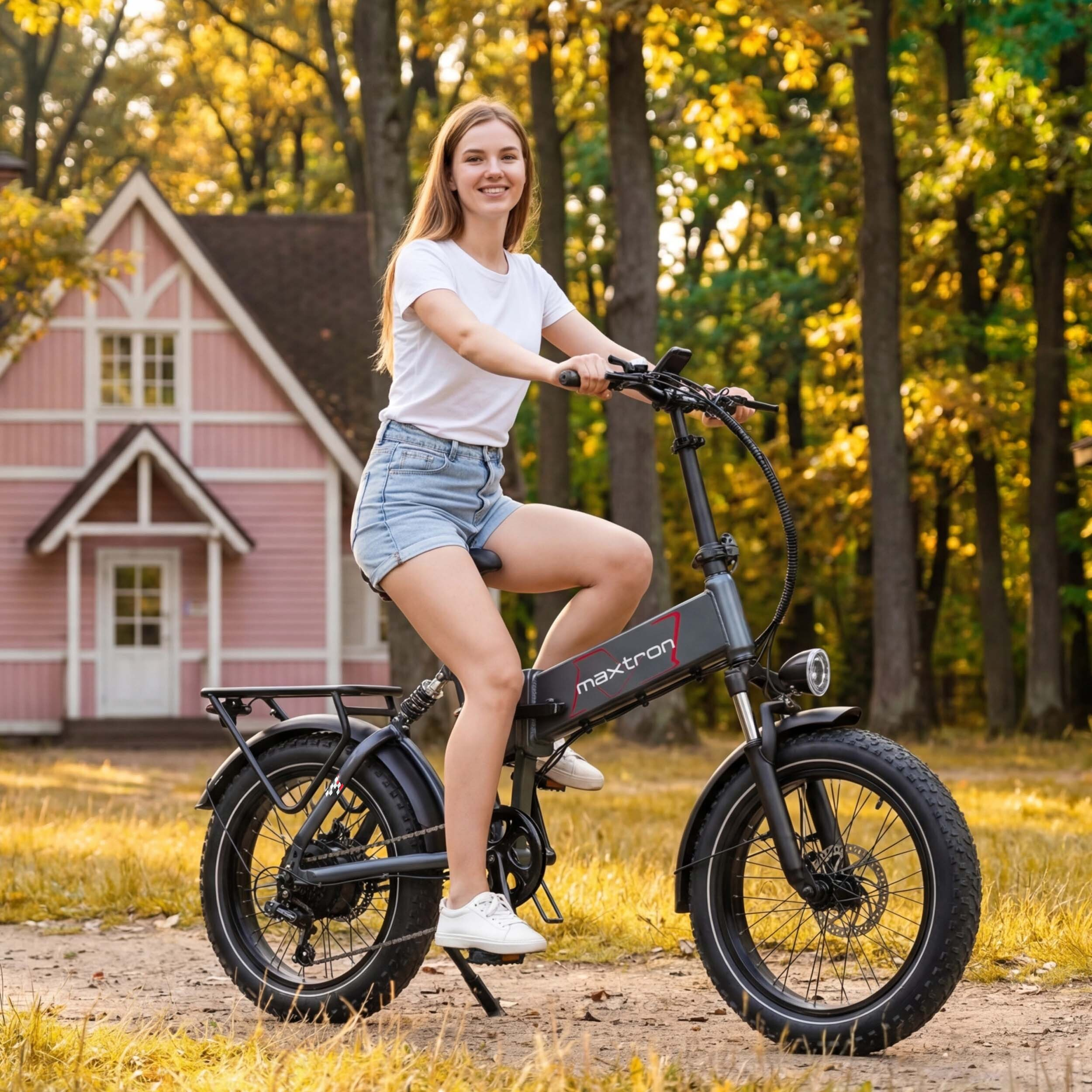 Kobieta jedzie rowerem elektrycznym przed różowym domem jesienią.