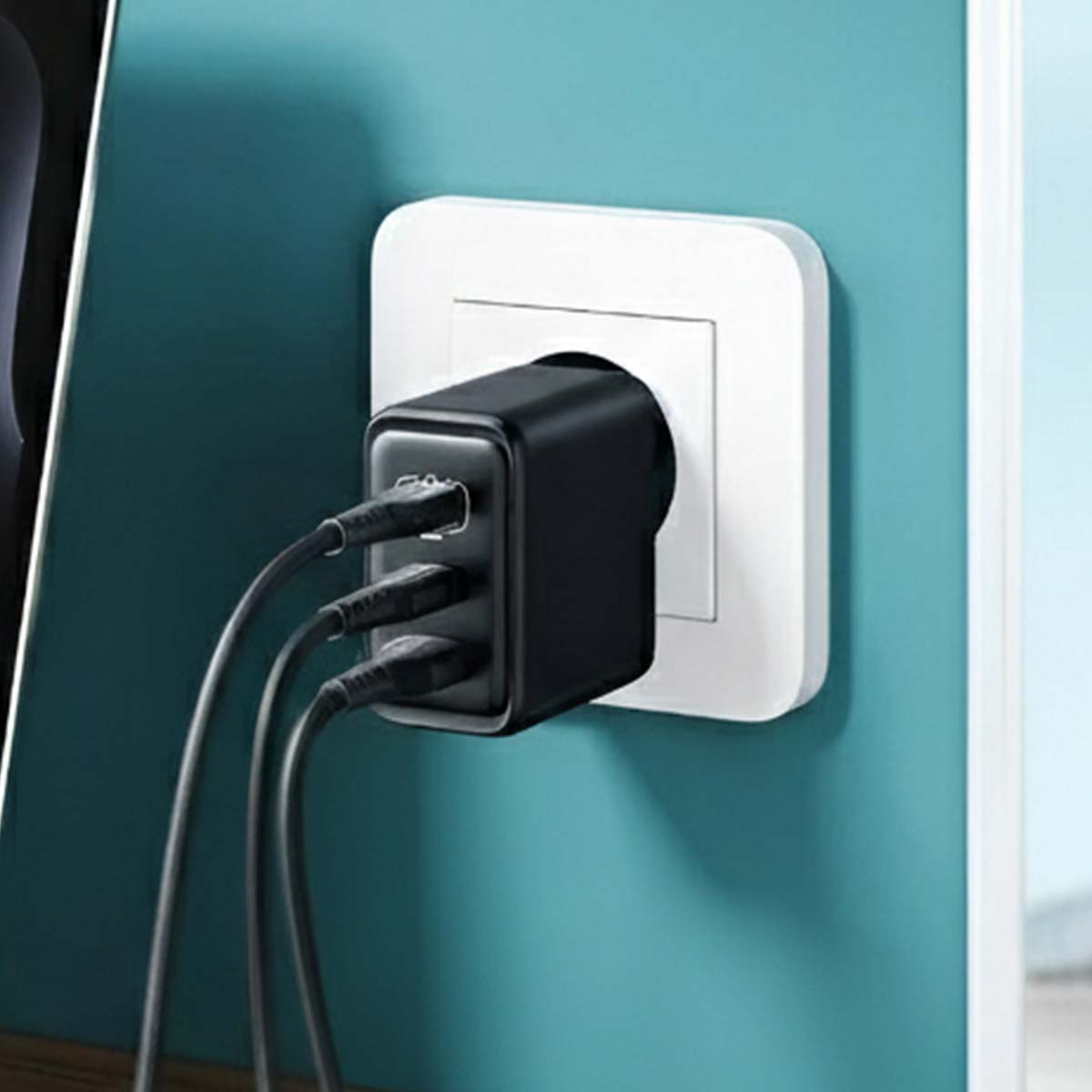 Caricatore USB nero multiport collegato a una presa a muro bianca. Tre cavi neri escono dal caricatore.