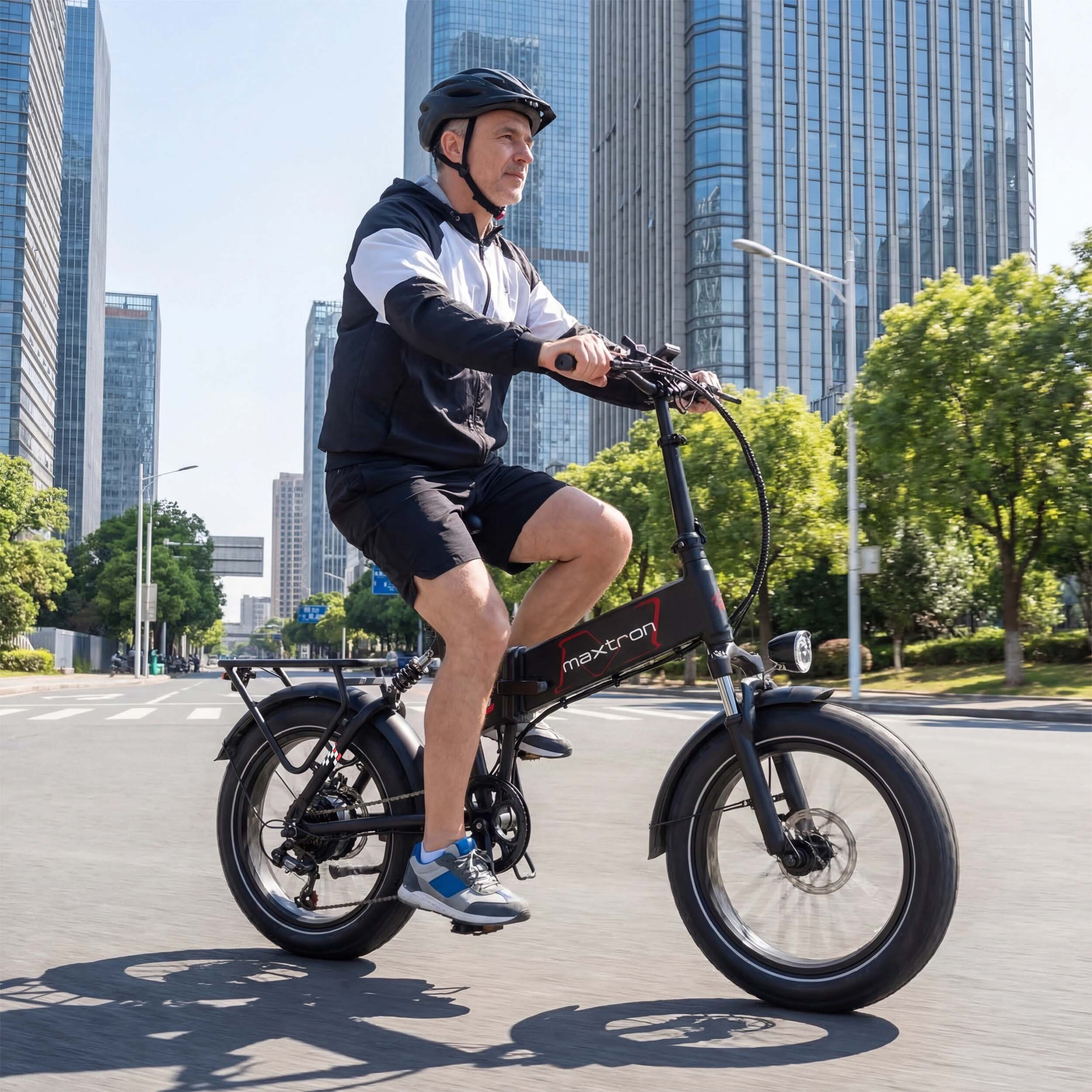 Mężczyzna w kasku jedzie czarnym rowerem elektrycznym po ulicy miasta z wysokimi budynkami.