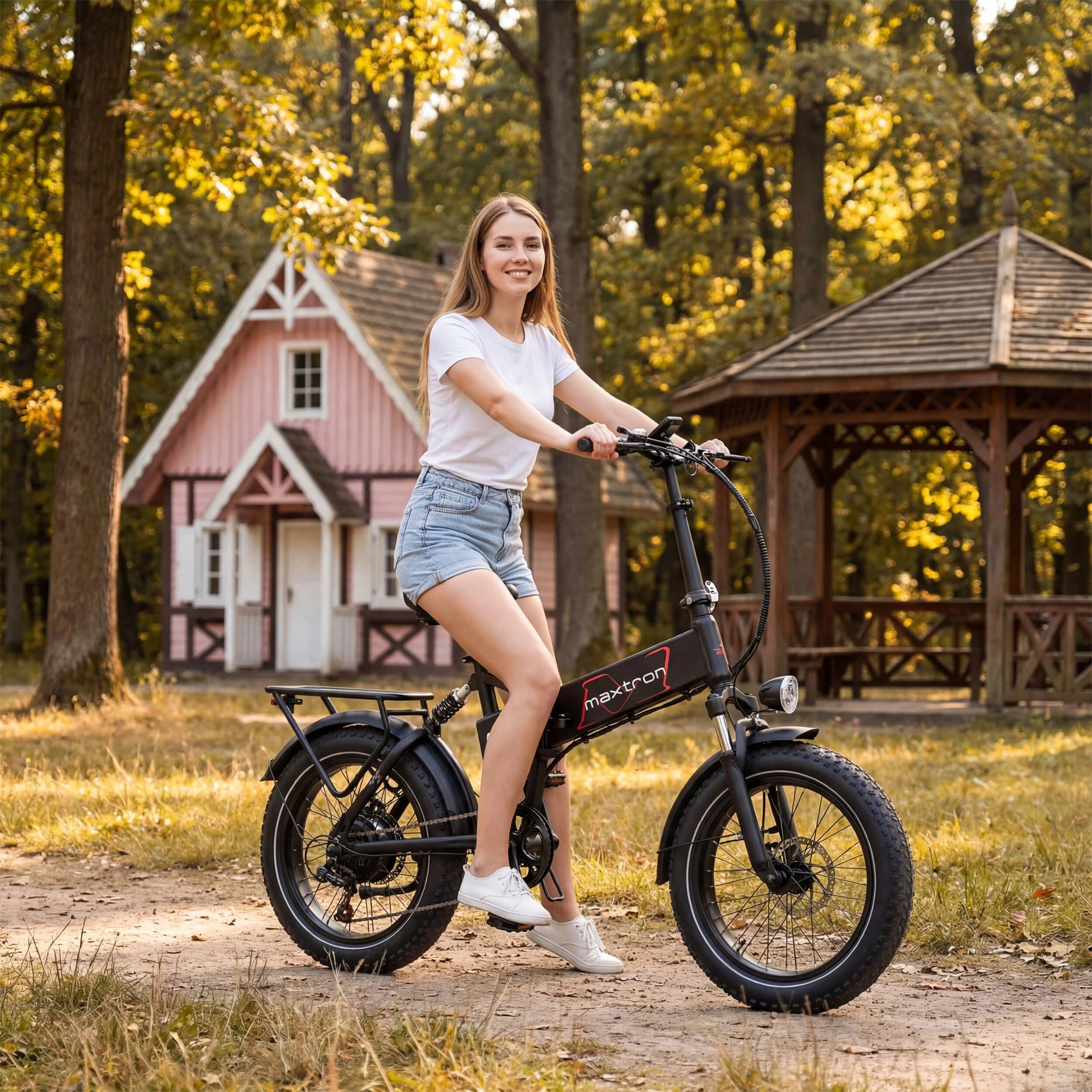 Kobieta jedzie na rowerze elektrycznym w parku z różowym domem i altaną.