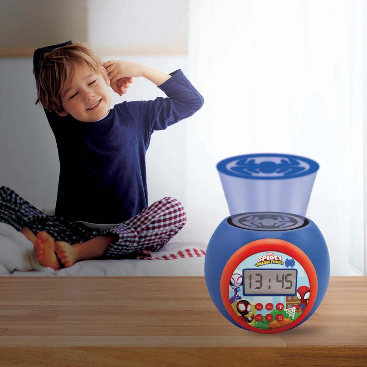 Ein Junge in Schlafanzug streckt sich auf einem Bett neben einem blauen Wecker mit Spiderman-Motiv.
