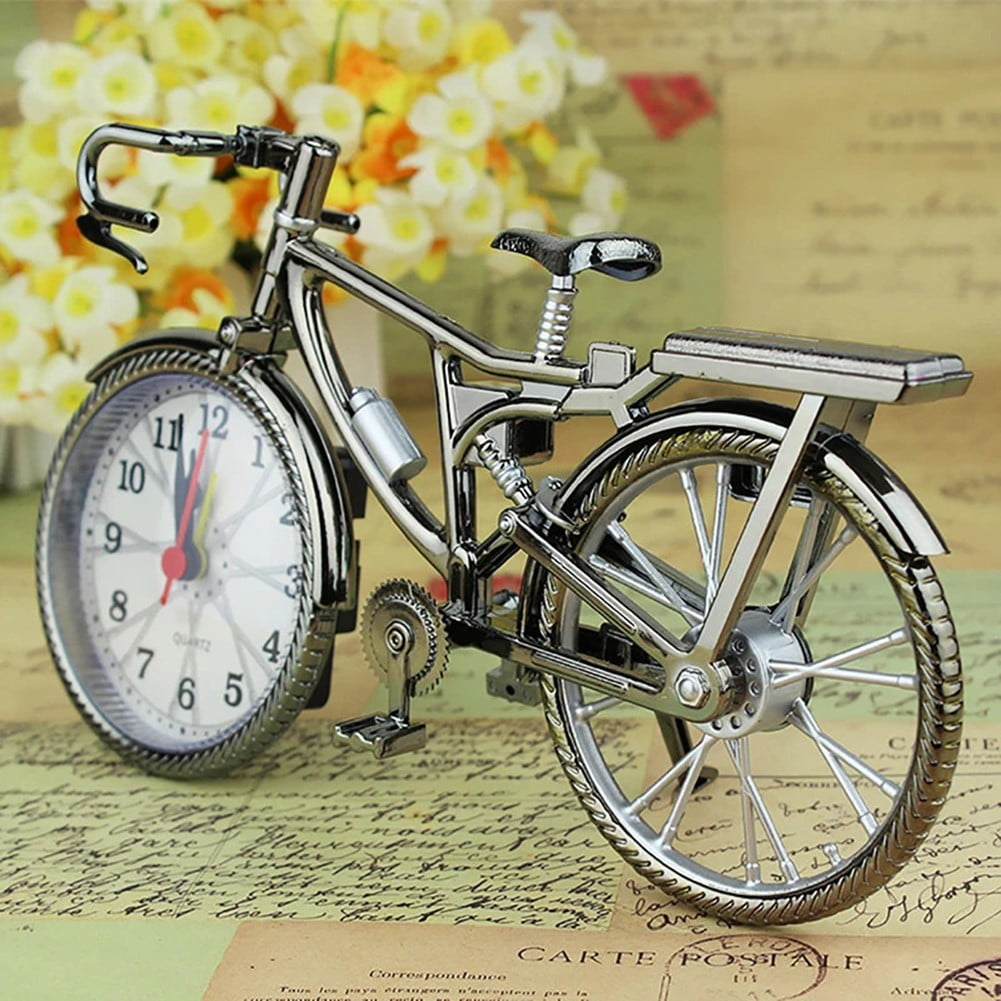 Silberner Fahrrad-Takt-Wecker auf Vintage-Papier mit Blumen im Hintergrund.
