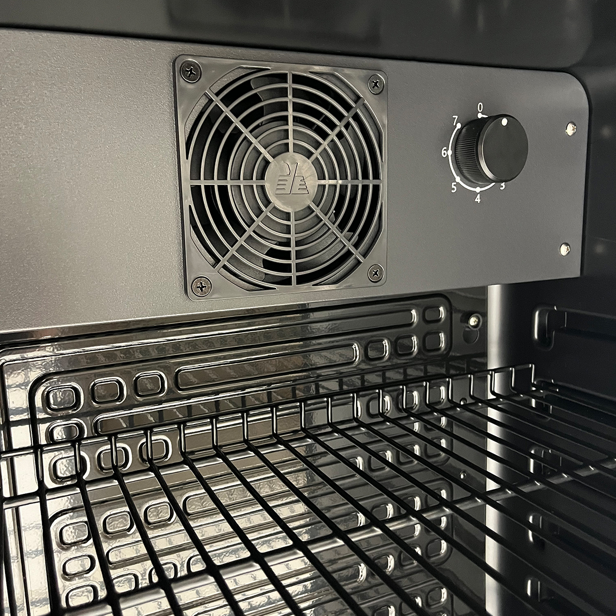 Een ventilator en een draaiknop zijn boven een ovenrooster gemonteerd.