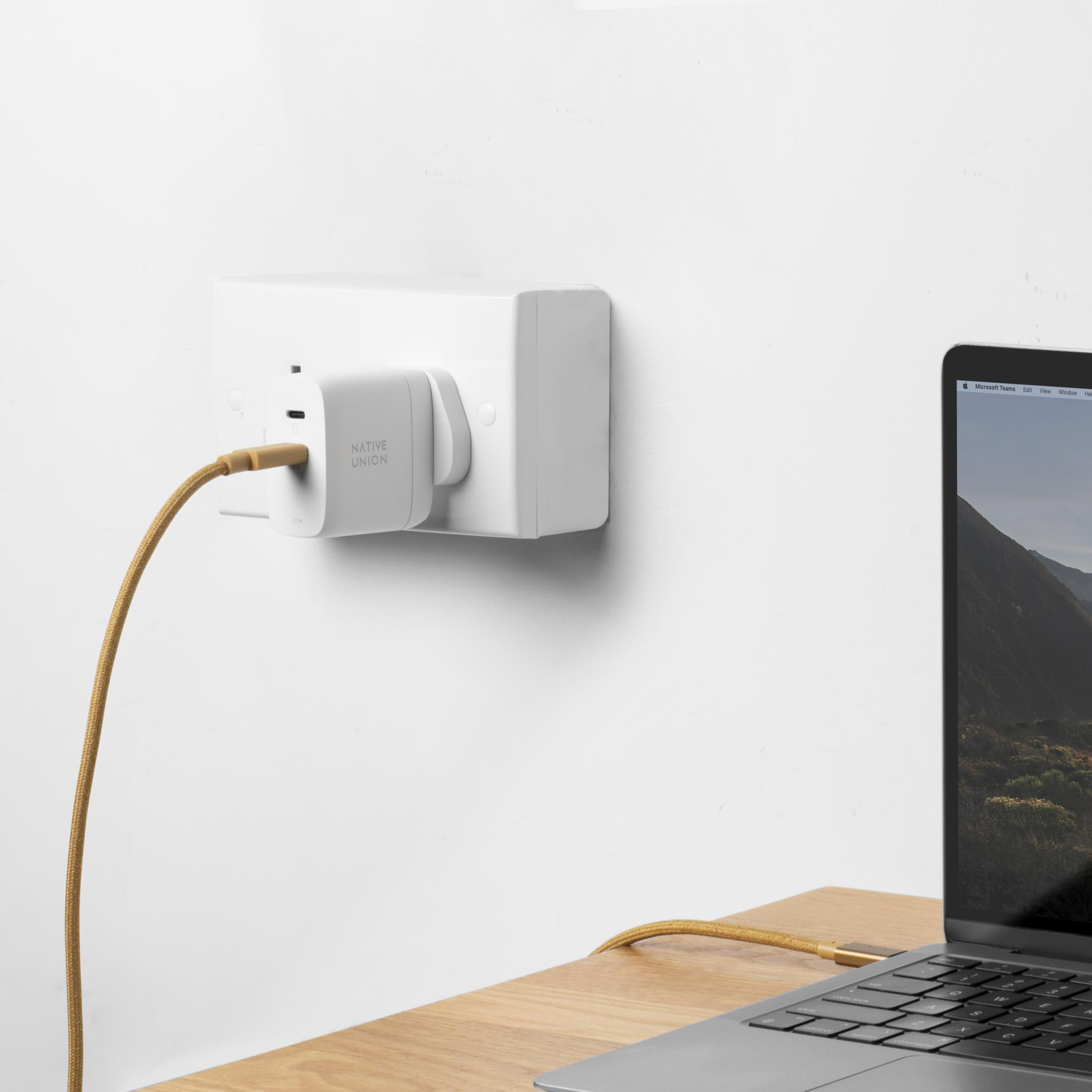 Ein weißer Netzstecker mit goldenem Kabel, das in einen Laptop gesteckt ist.