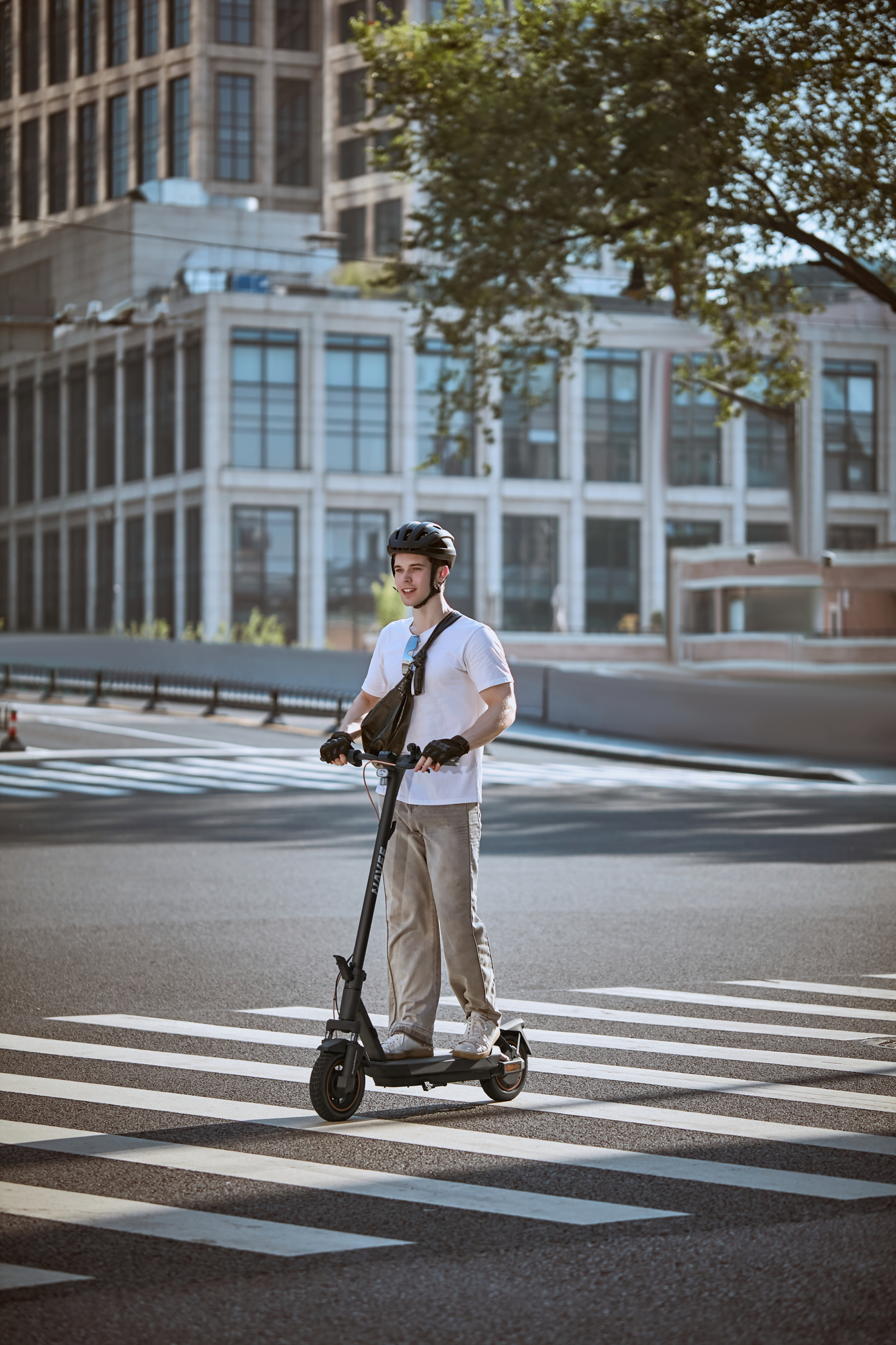 Un hombre en un patinete eléctrico cruza un paso de peatones frente a un edificio.