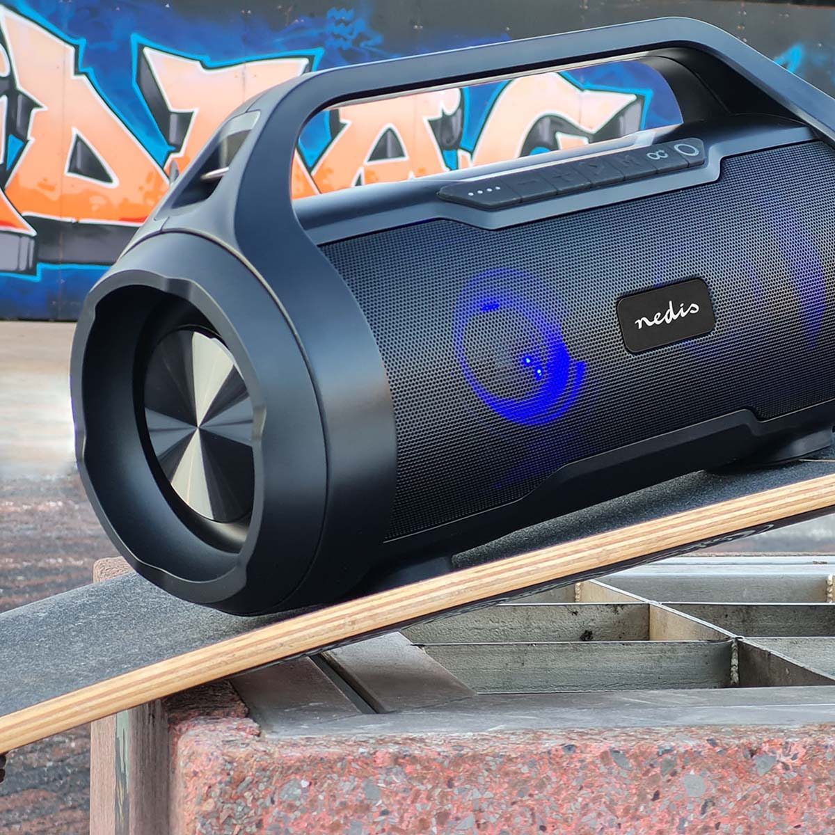 Altoparlante Bluetooth nero con manico su skateboard davanti a muro di graffiti.