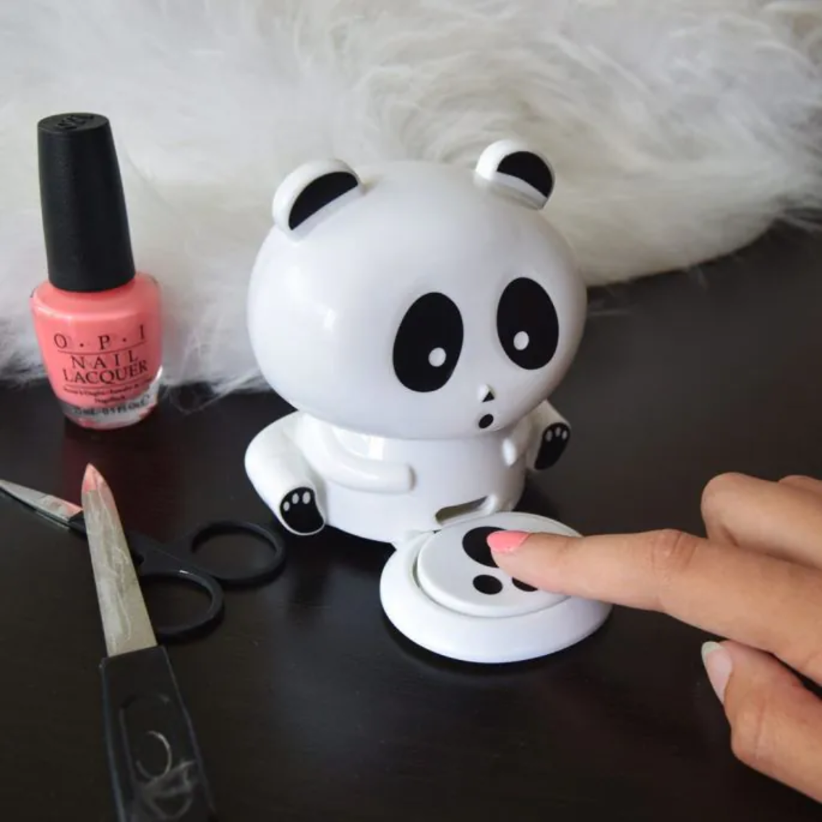 A panda-shaped nail polish dispenser with a hand pressing a button.