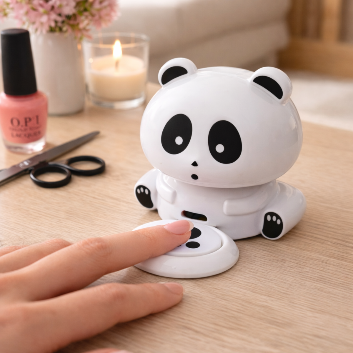 A panda device on a wooden table with nail polish, candle, and scissors.